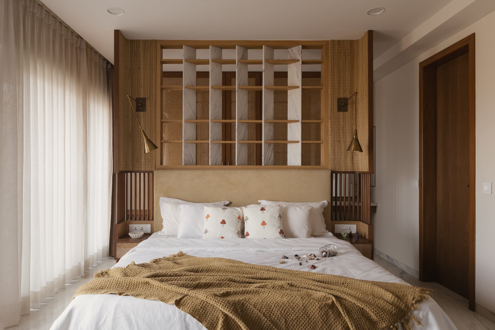The second bedroom's headboard wall, composed of marble-and-oak gridded shelving, cane panels and articulated brass sconces