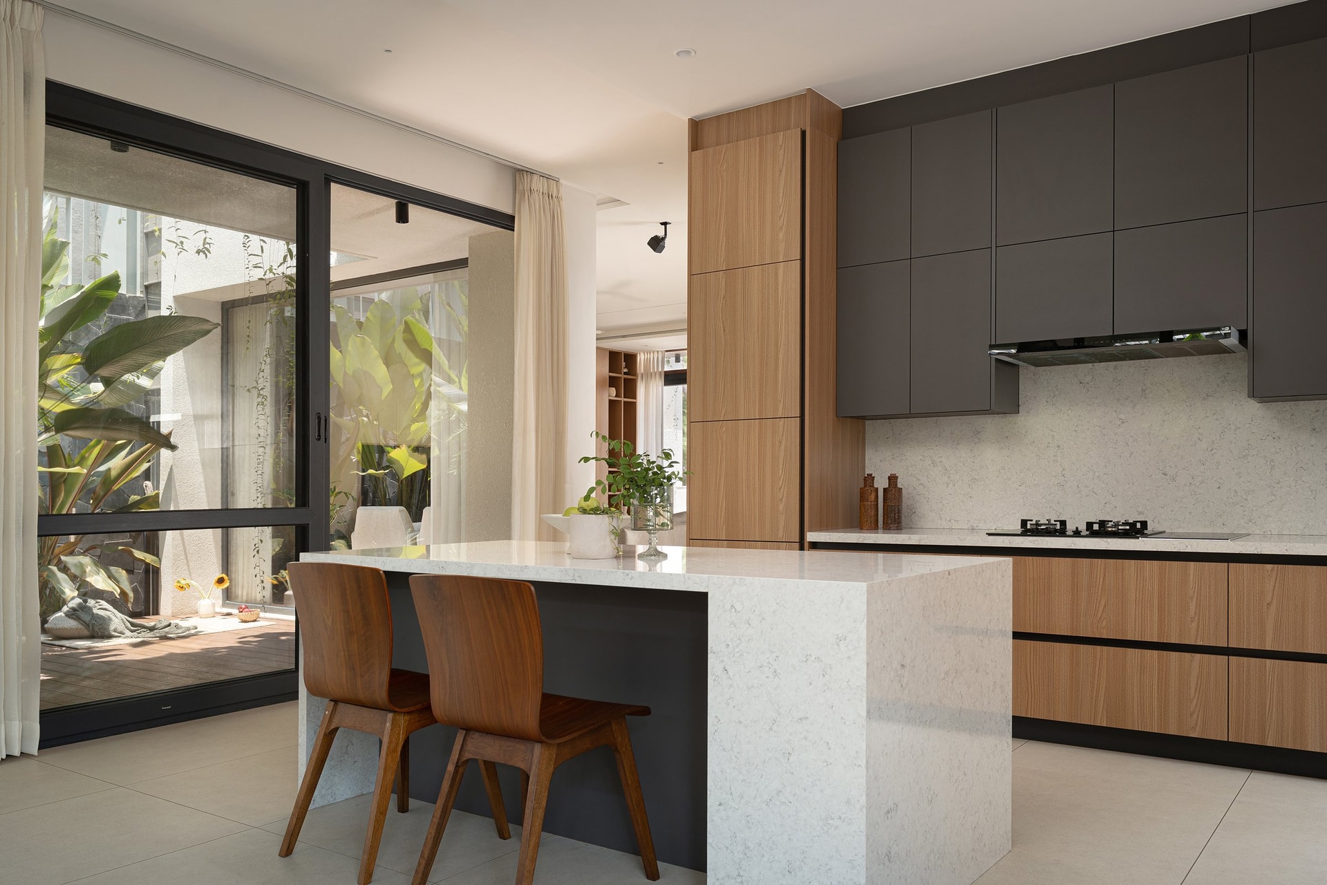 The kitchen, its pale veined island paired with dark matte upper cabinetry and warm timber base units