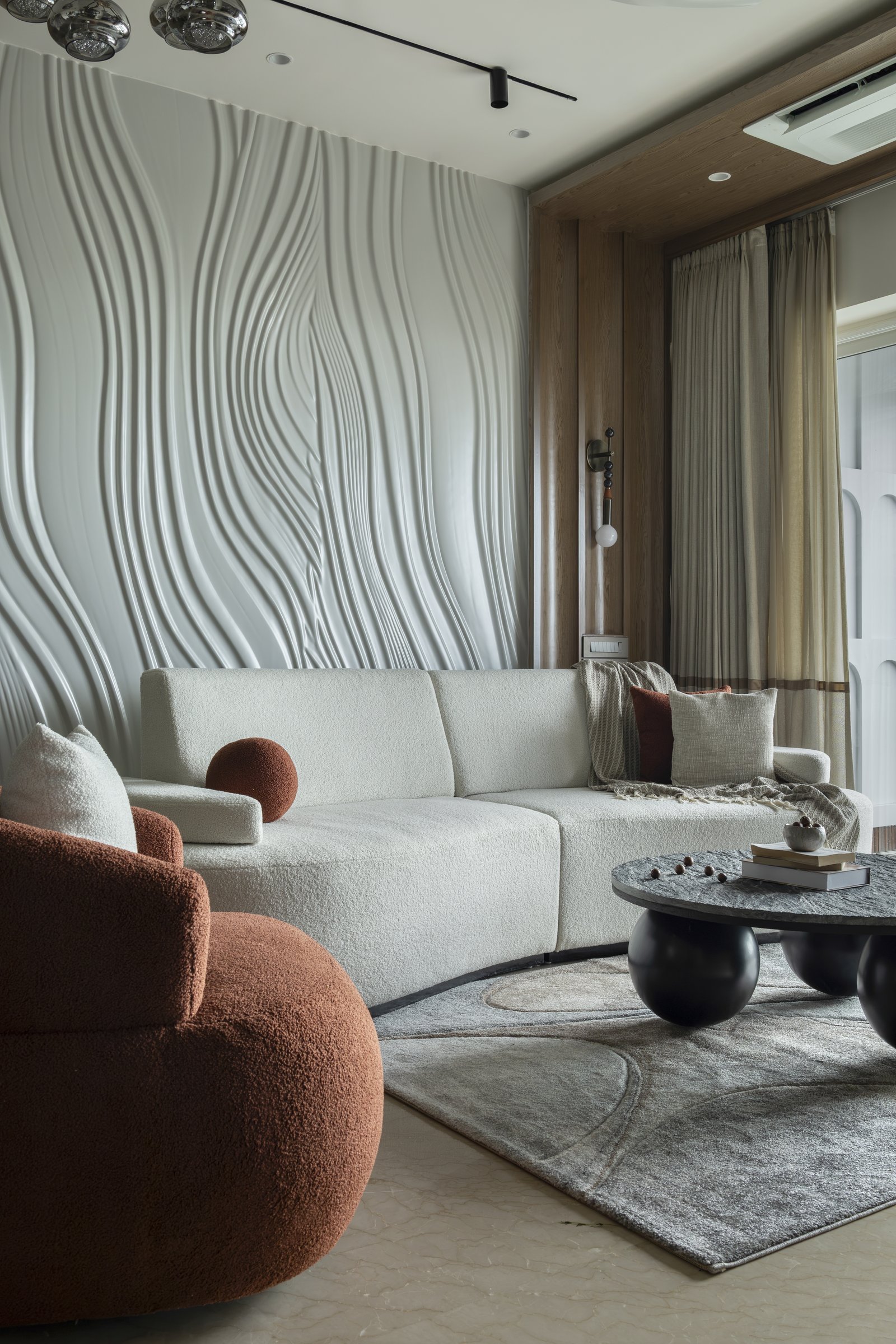 The living room, where a sculpted wave-form wall catches shifting light behind pale bouclé seating and a rounded black coffee table