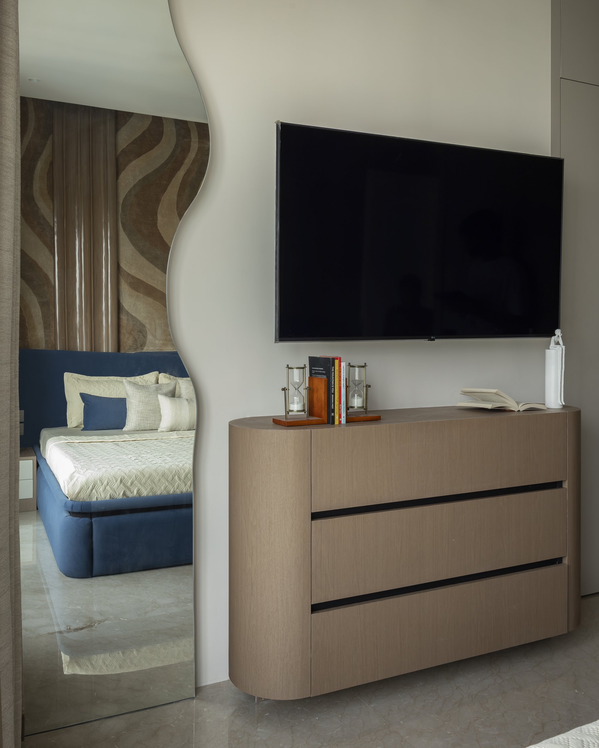 The curved veneered dresser opposite the bed, chosen to reduce the visual heaviness of storage