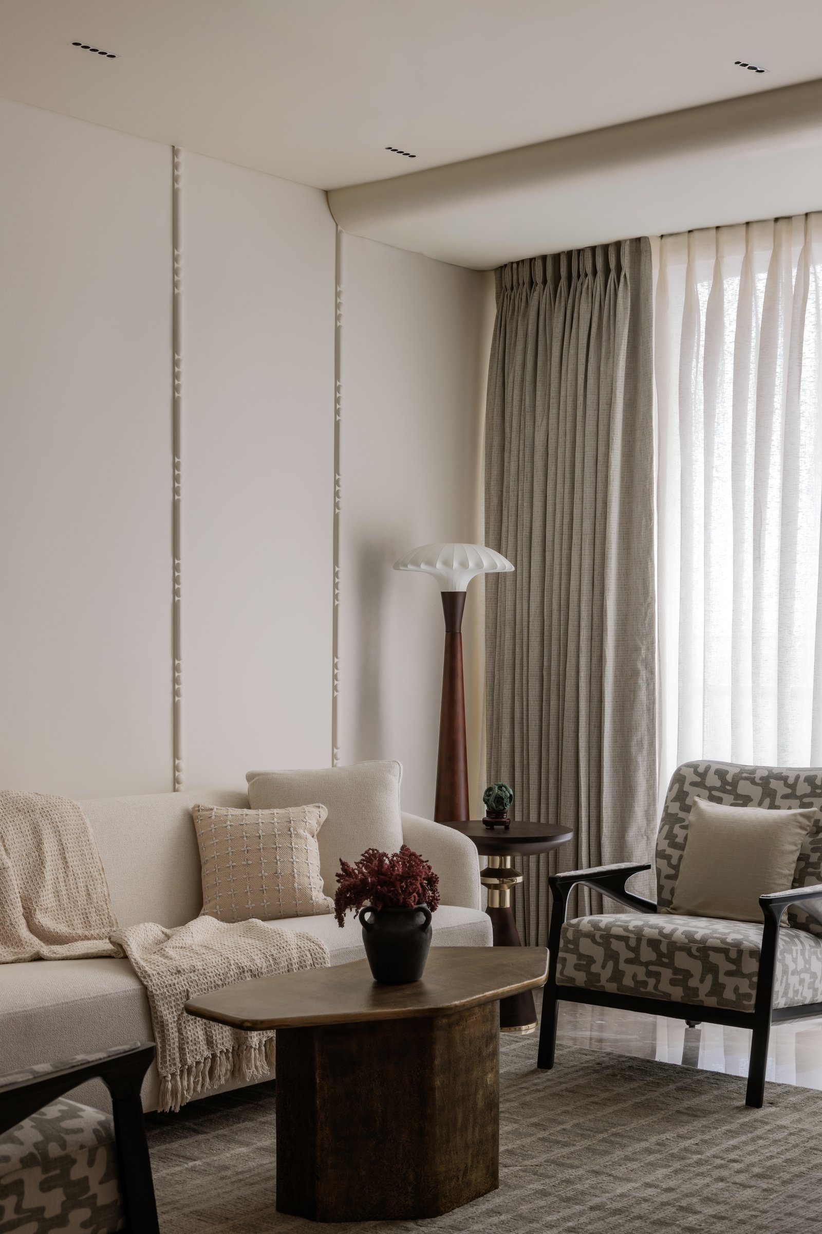 The living room seating, arranged around a sculptural metal coffee table beneath pinch-pleat drapery that filters the city light
