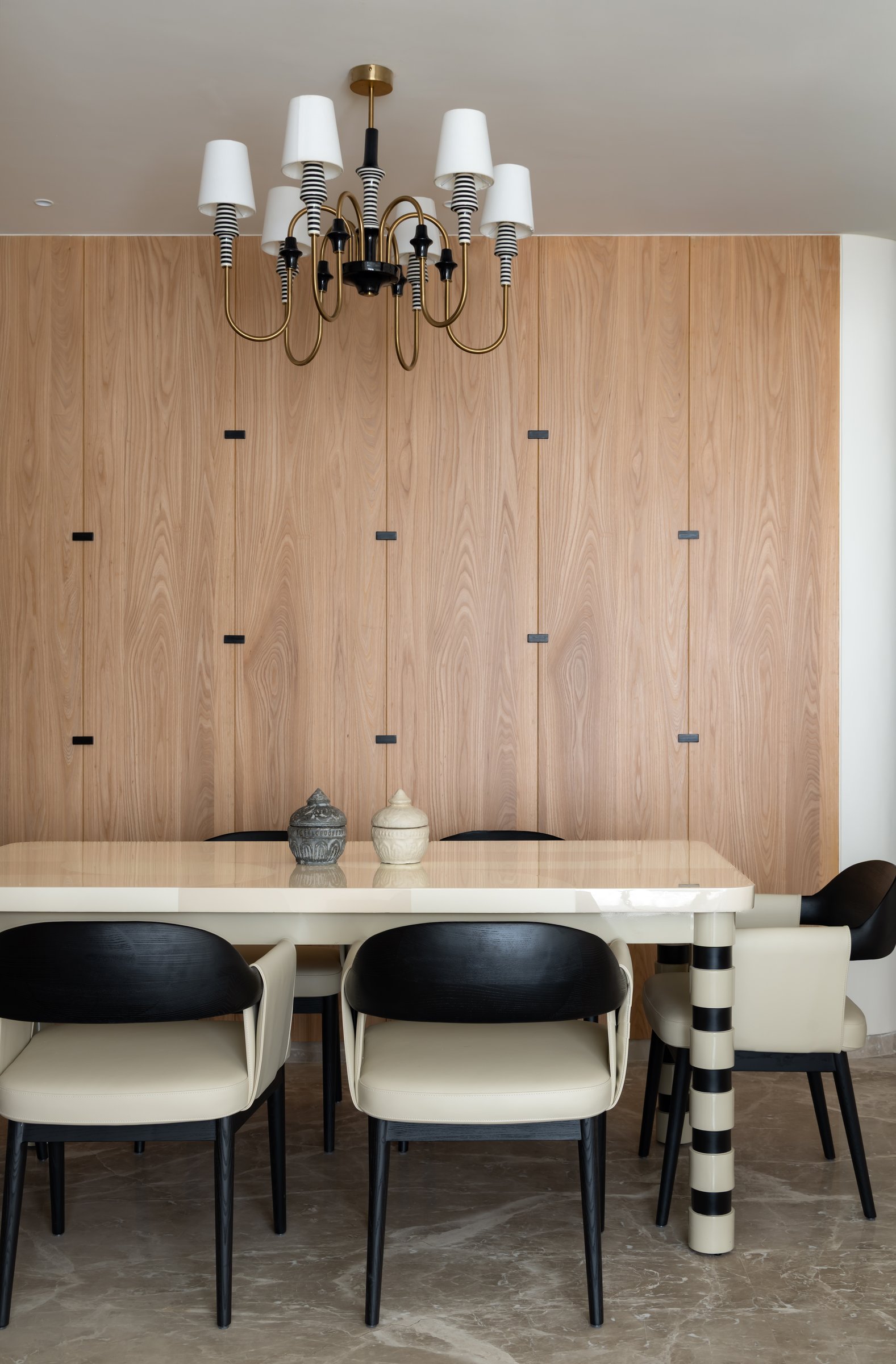 The dining area, where a cream lacquered table with striped legs sits beneath a chandelier of striped candle sleeves on brass arms