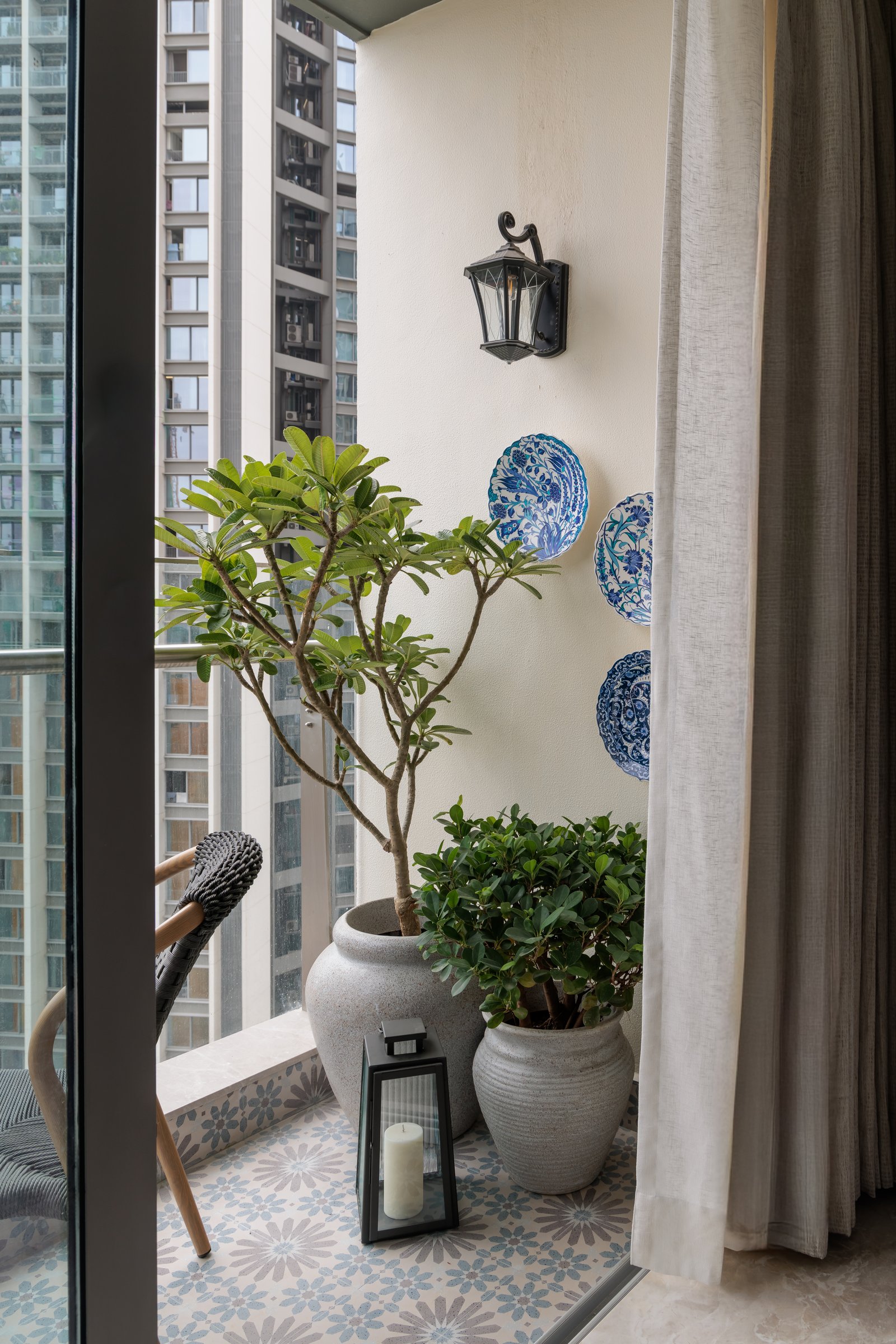 The balcony, laid in a soft blue-and-cream patterned tile with hand-painted ceramic plates beside a lantern-style sconce
