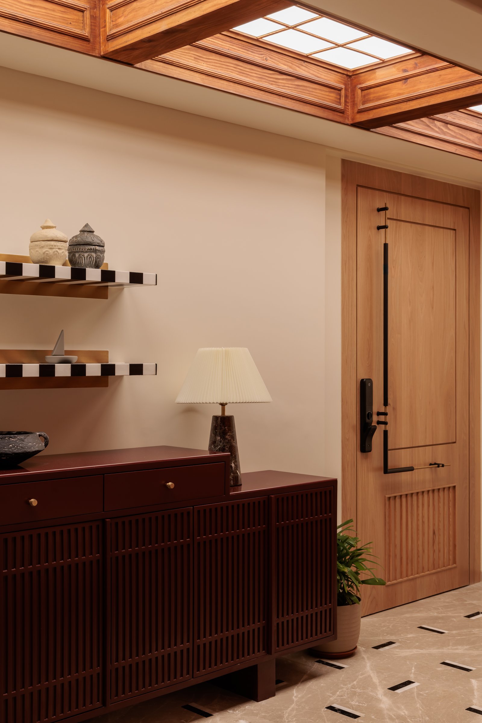 The oxblood console with slim fluted doors, floating striped shelves and a panelled veneer entry door completing the foyer composition