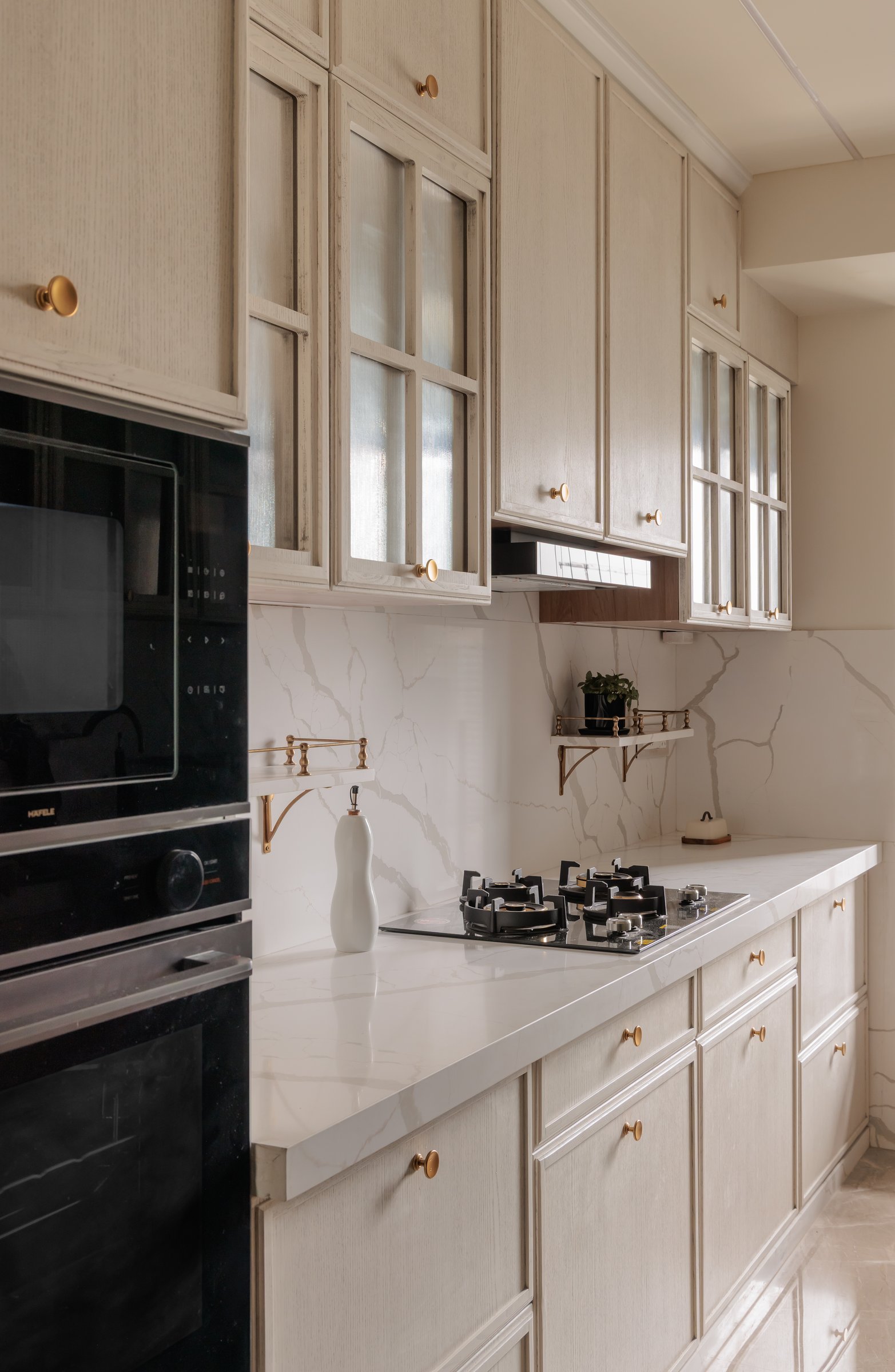 The working kitchen, with pale mullioned cabinetry, brass gallery shelves and a book-matched marble backsplash