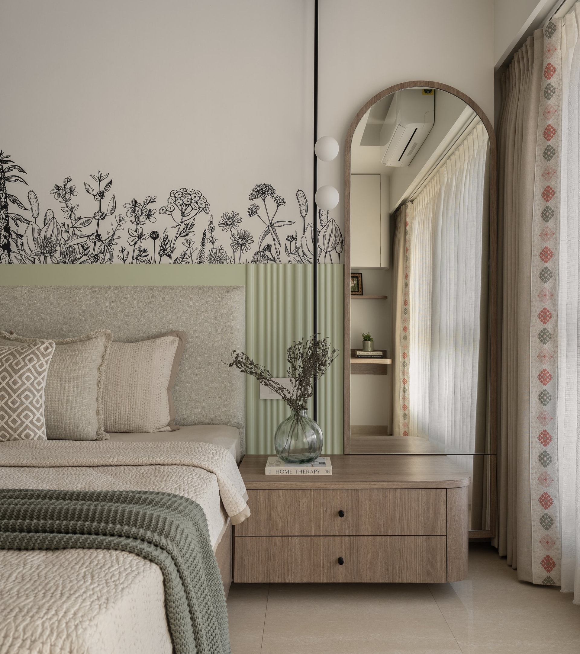 An arched floor mirror and wooden bedside chest, with a patterned curtain edge adding folk inflection