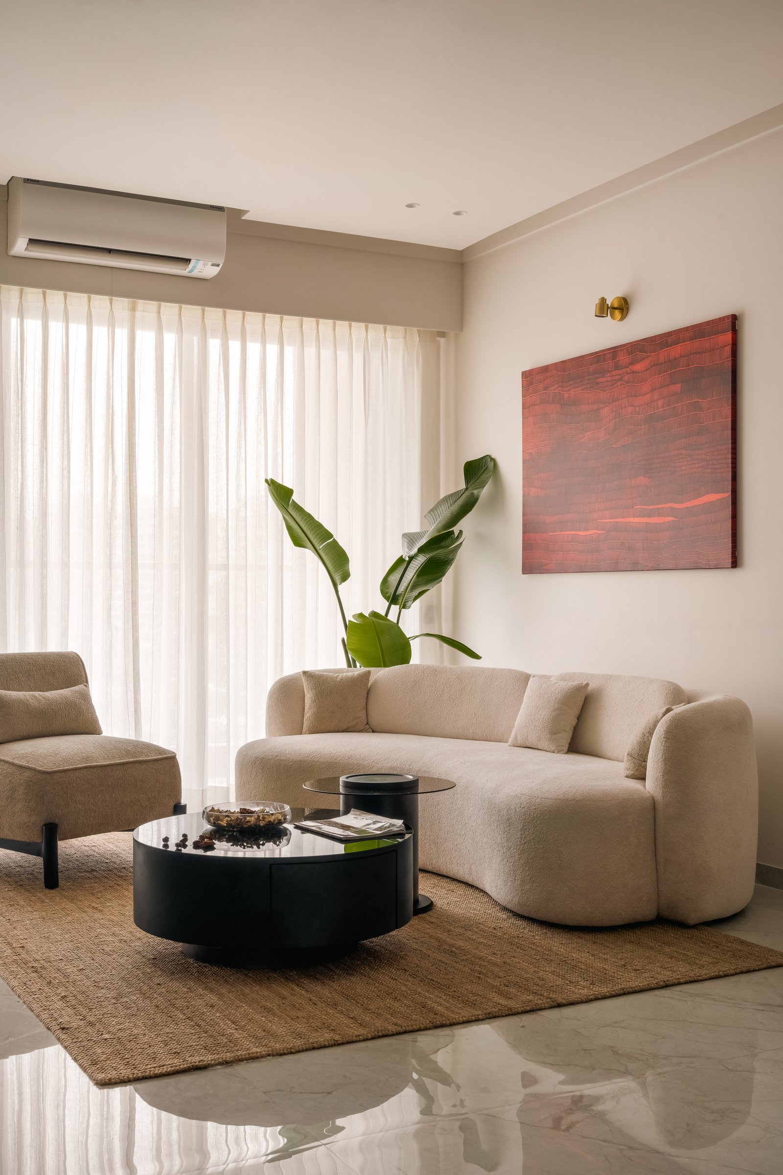 A curved bouclé sofa and dark circular tables anchor the living room, with a single red artwork providing the only saturated note