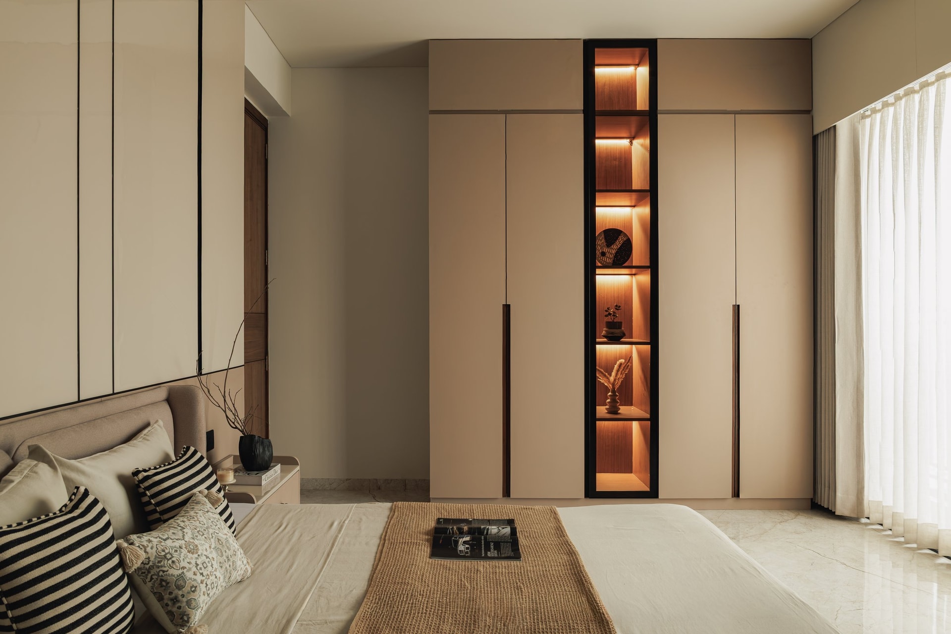 The master bedroom, where a tall backlit niche of wooden shelving interrupts the beige wardrobe wall