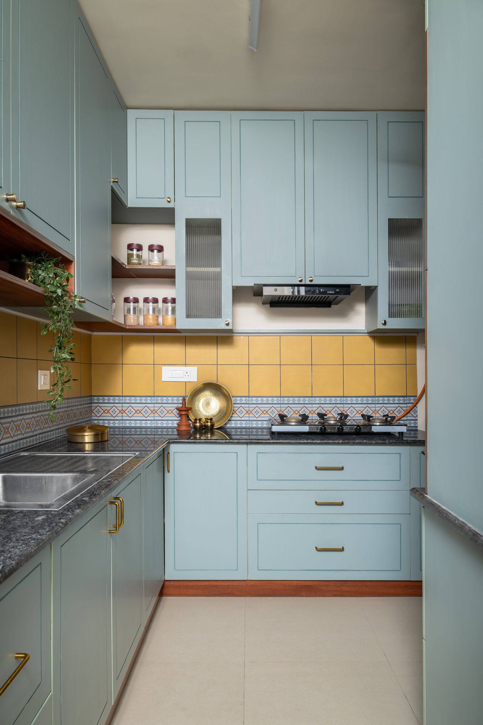 The kitchen, where muted blue-green shaker cabinetry meets a mustard-yellow tiled backsplash with a patterned border