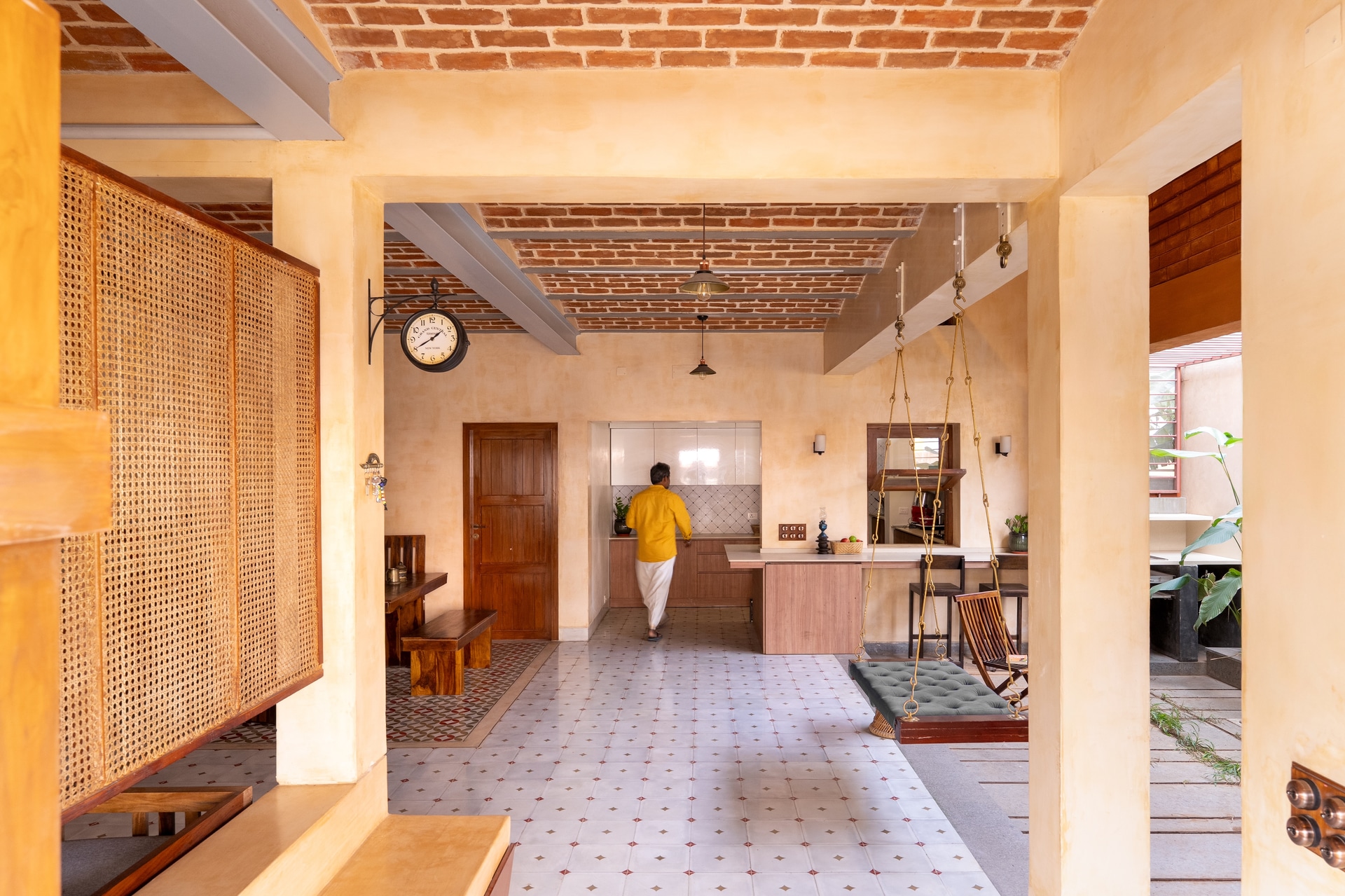 The central hall of House of Slow Reflections in Chennai, with an exposed brick ceiling, a cane screen and a swing seat on the axis.