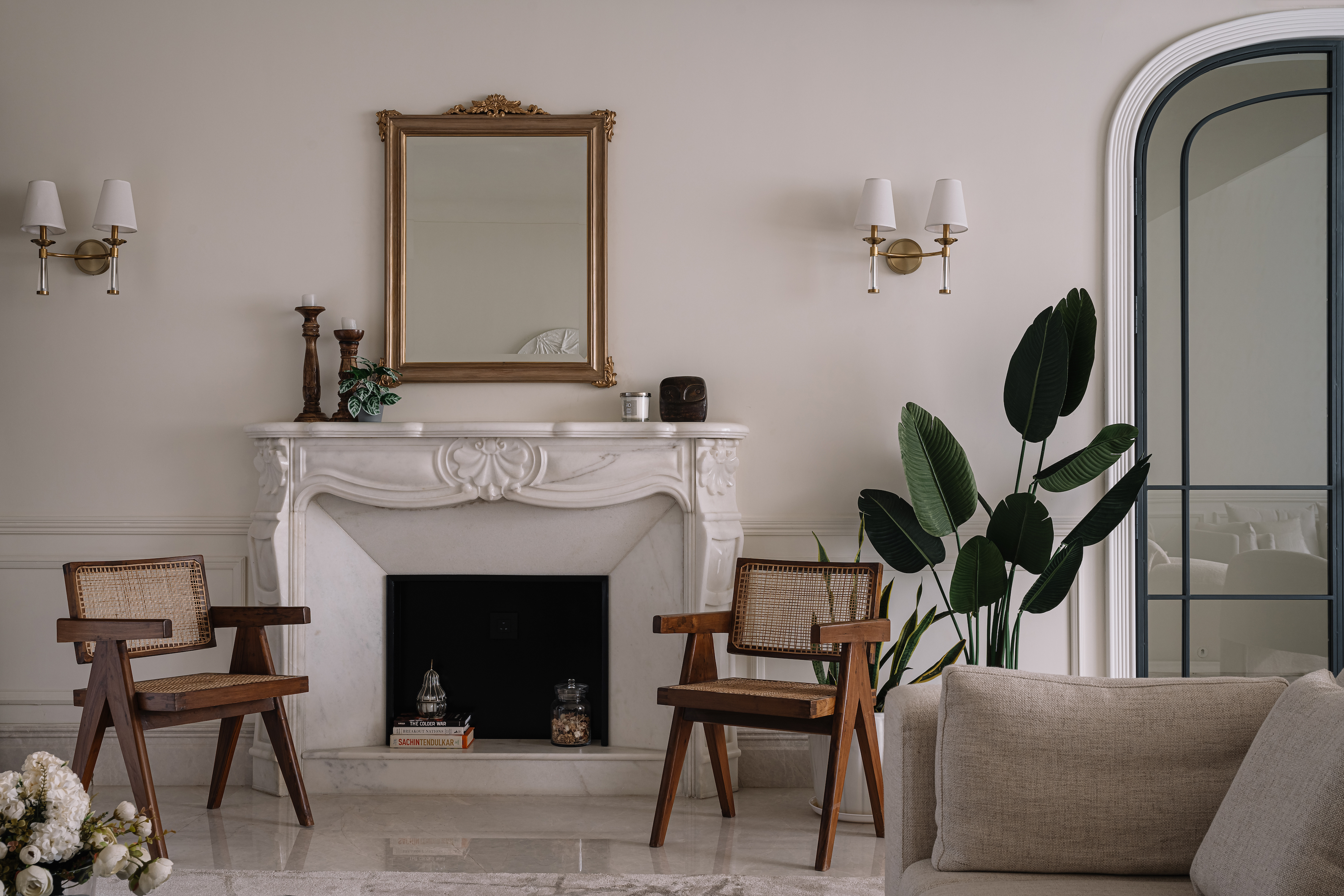 Living room with carved marble fireplace, gilt mirror, cane armchairs and large plant