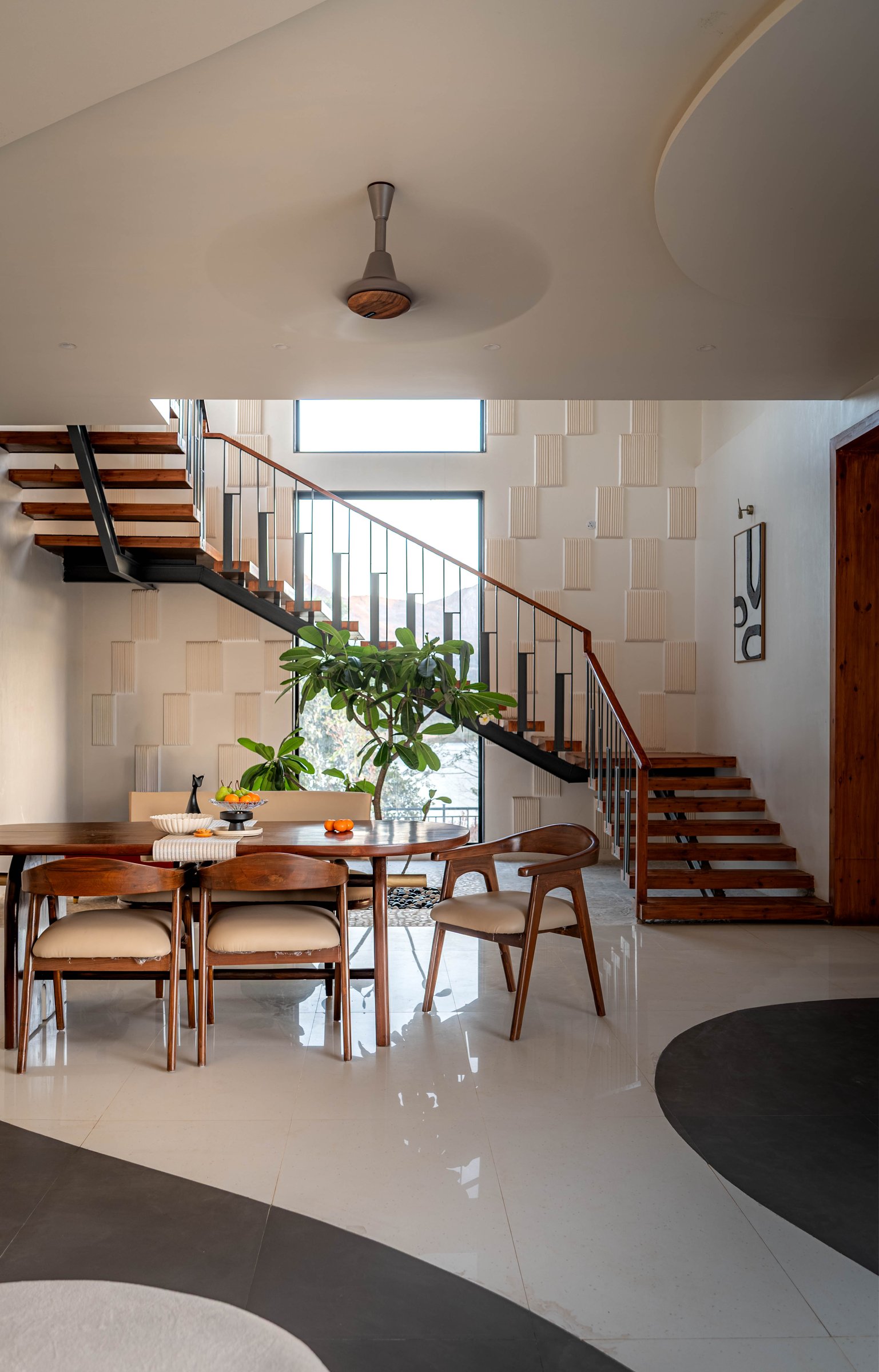 The dining area beneath the open stairwell, solid teak furniture set against a rhythmic textured wall