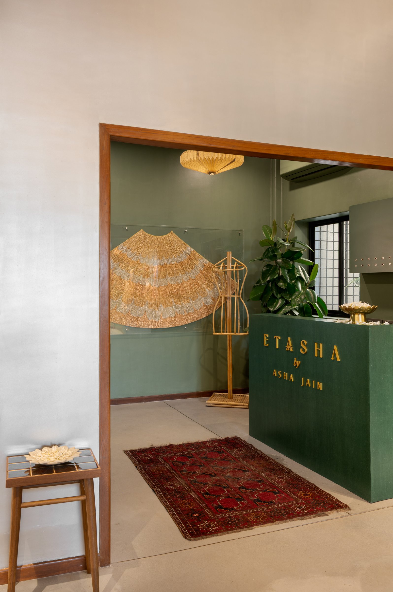 The entry threshold: a timber-framed opening reveals the emerald reception volume, with the Etasha wordmark set against pigmented green