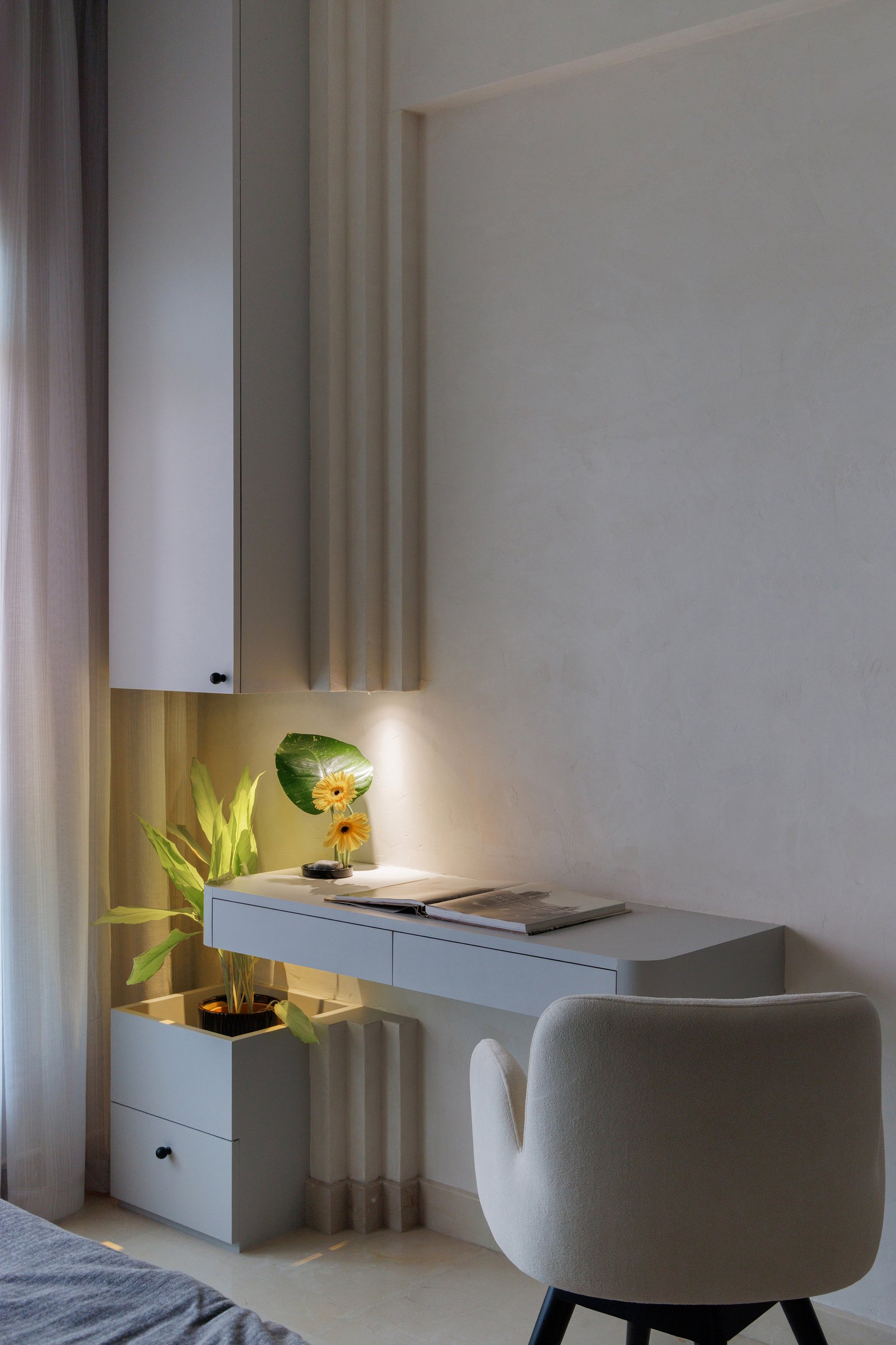 A compact writing nook beside the bed: a pale lacquered desk floats from the wall, its fluted side panel scaling down the apartment's larger architectural language