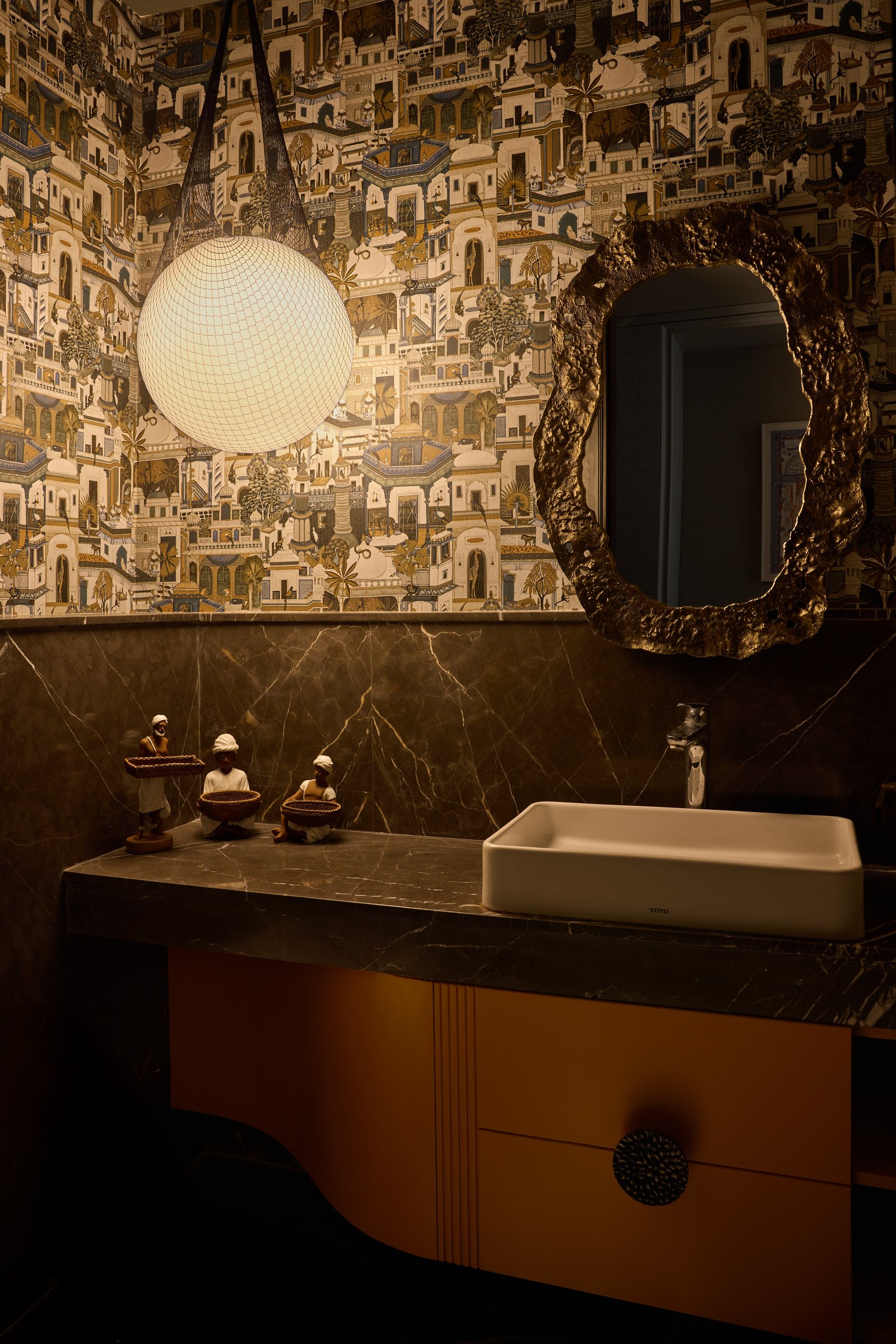 The powder room, where patterned wallpaper and a bronze-framed textured mirror break the apartment's restraint