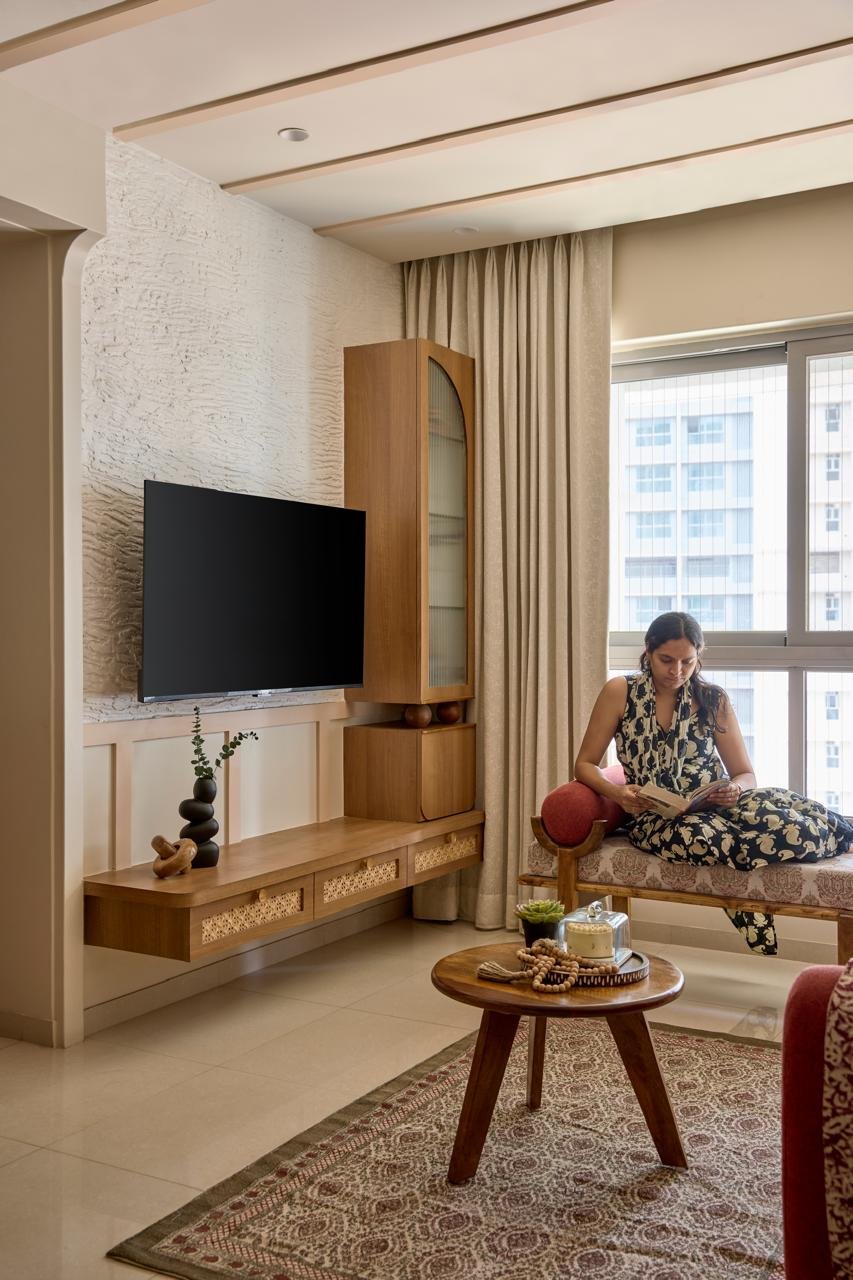 The media wall, where a textured ivory plaster surface meets a cane-fronted wooden console and an arched glass cabinet