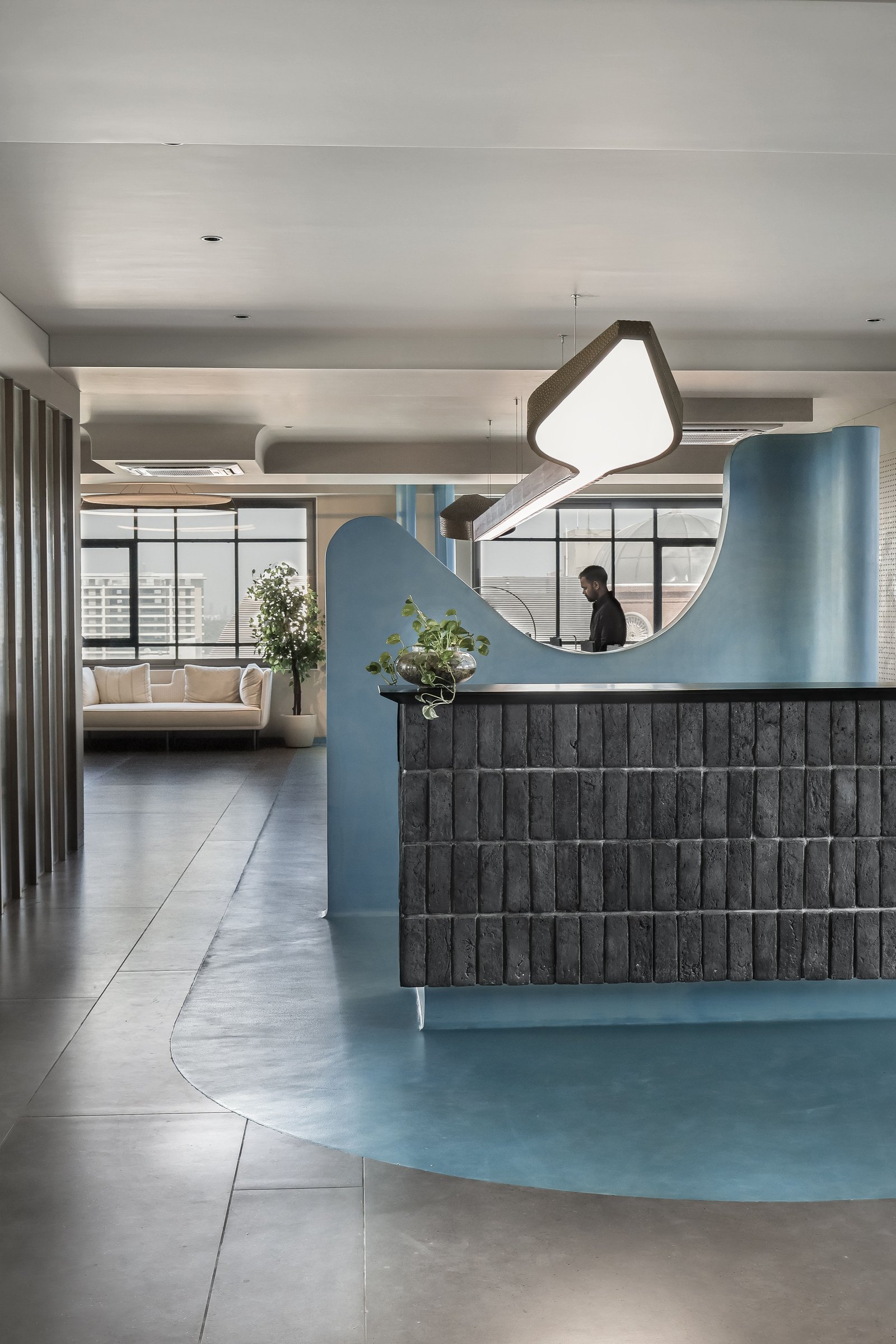 The reception read from the side, where the blue plinth, painted curve and perforated pendant compose a single sculptural choreography