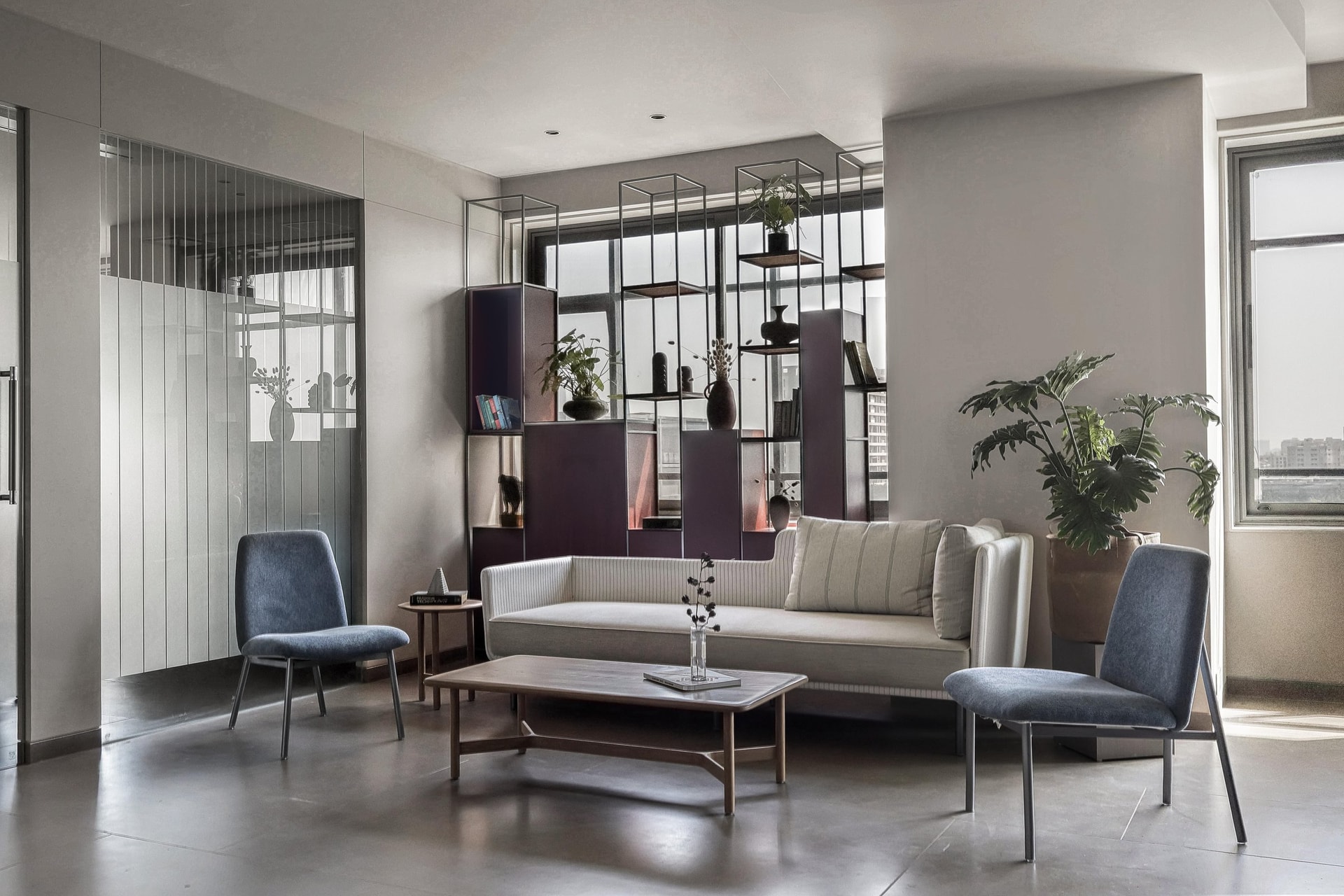 The lounge: striped upholstery, slate-blue armchairs, and a metal-framed open shelving wall set a confidently corporate tone