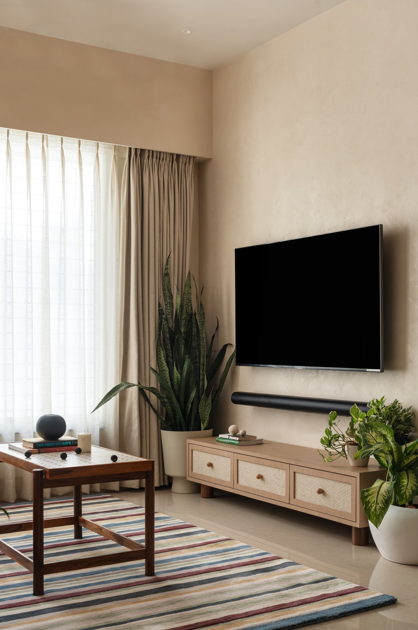 The media wall, kept almost bare so the rug and coffee table can carry the room's chromatic load