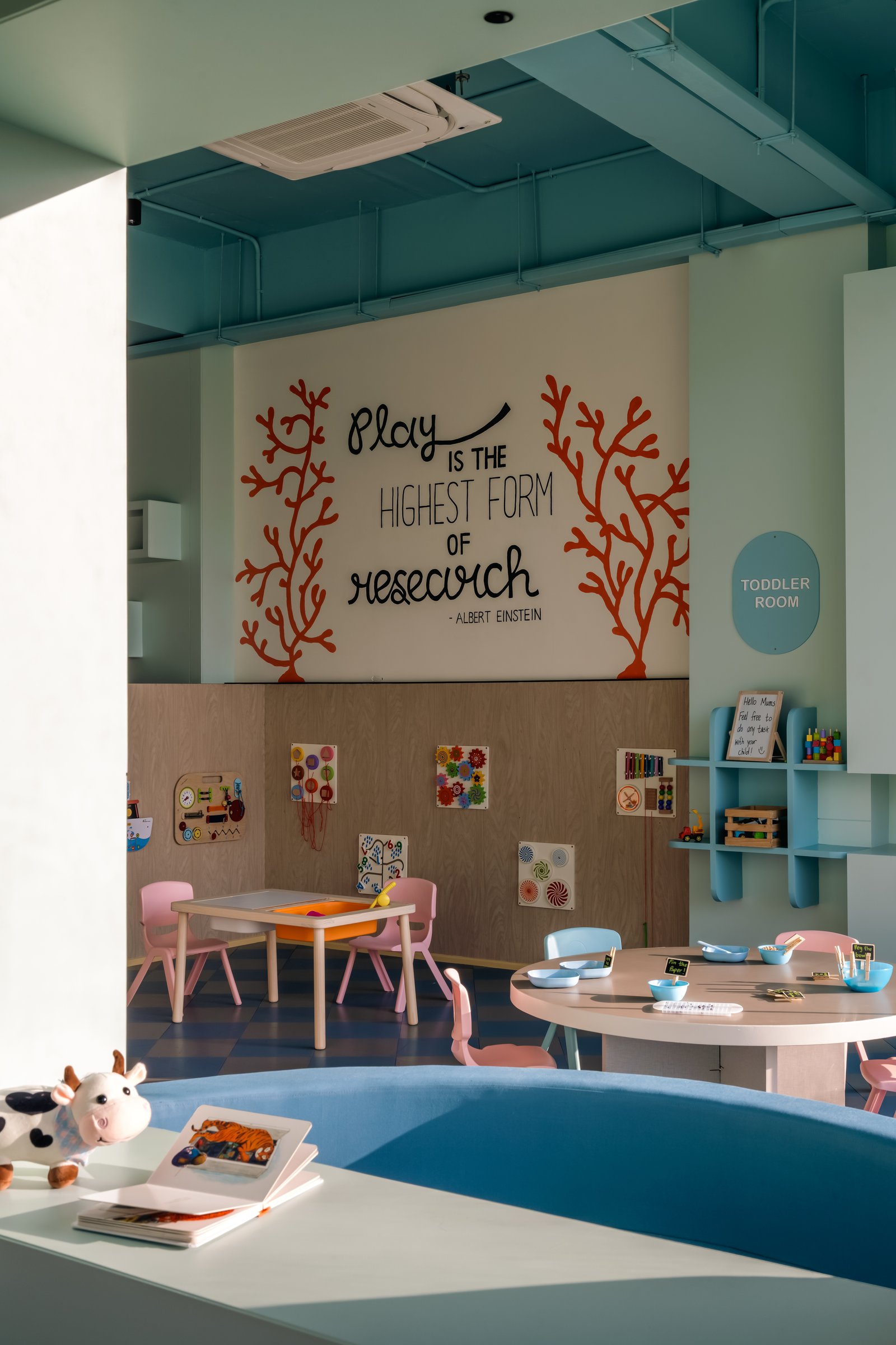 The toddler room: coral-branch motifs flank a hand-painted Einstein quote, the project's namesake made explicit