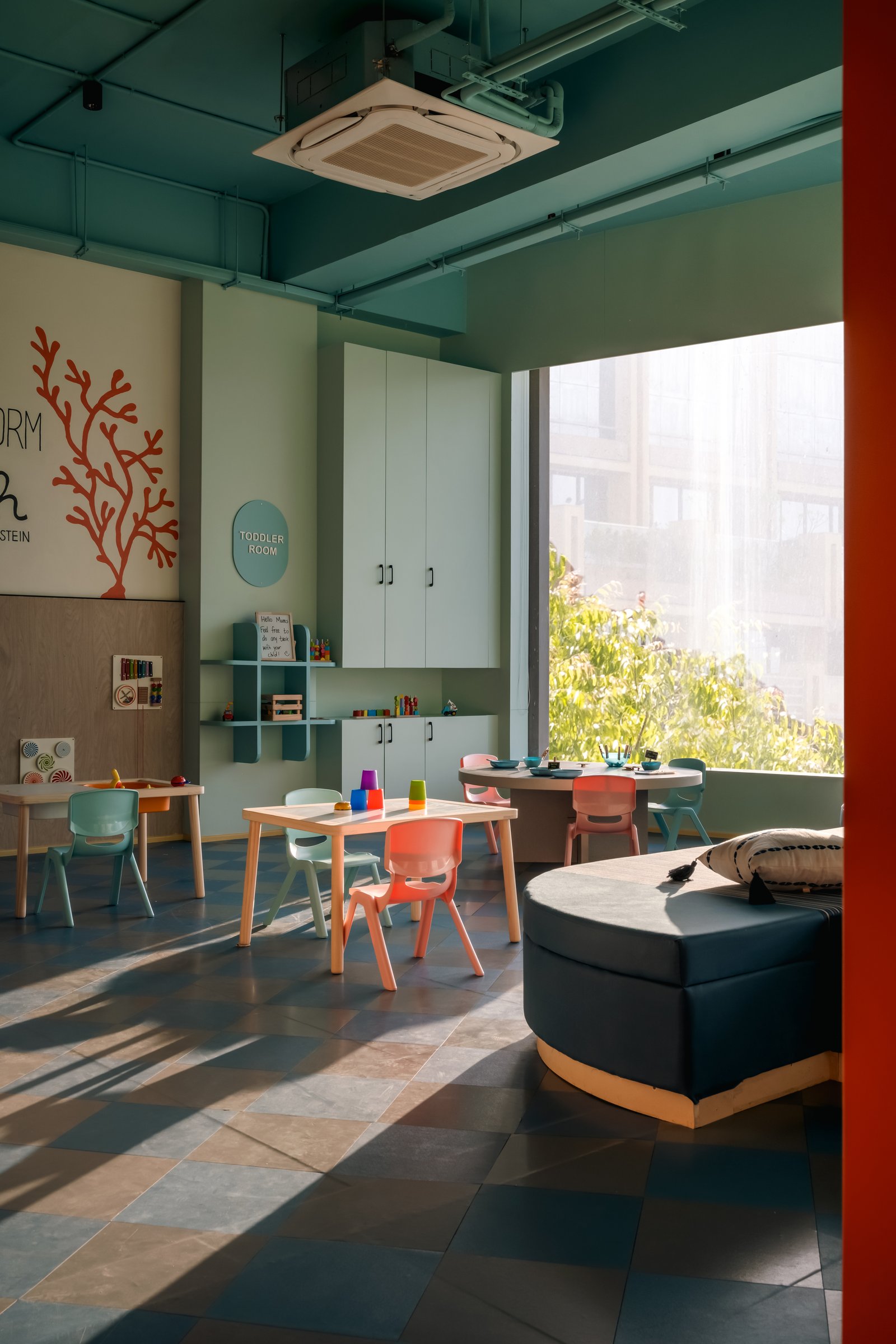 Mint cabinetry and a navy daybed in the toddler room, calm in colour temperature even as the programme is busy