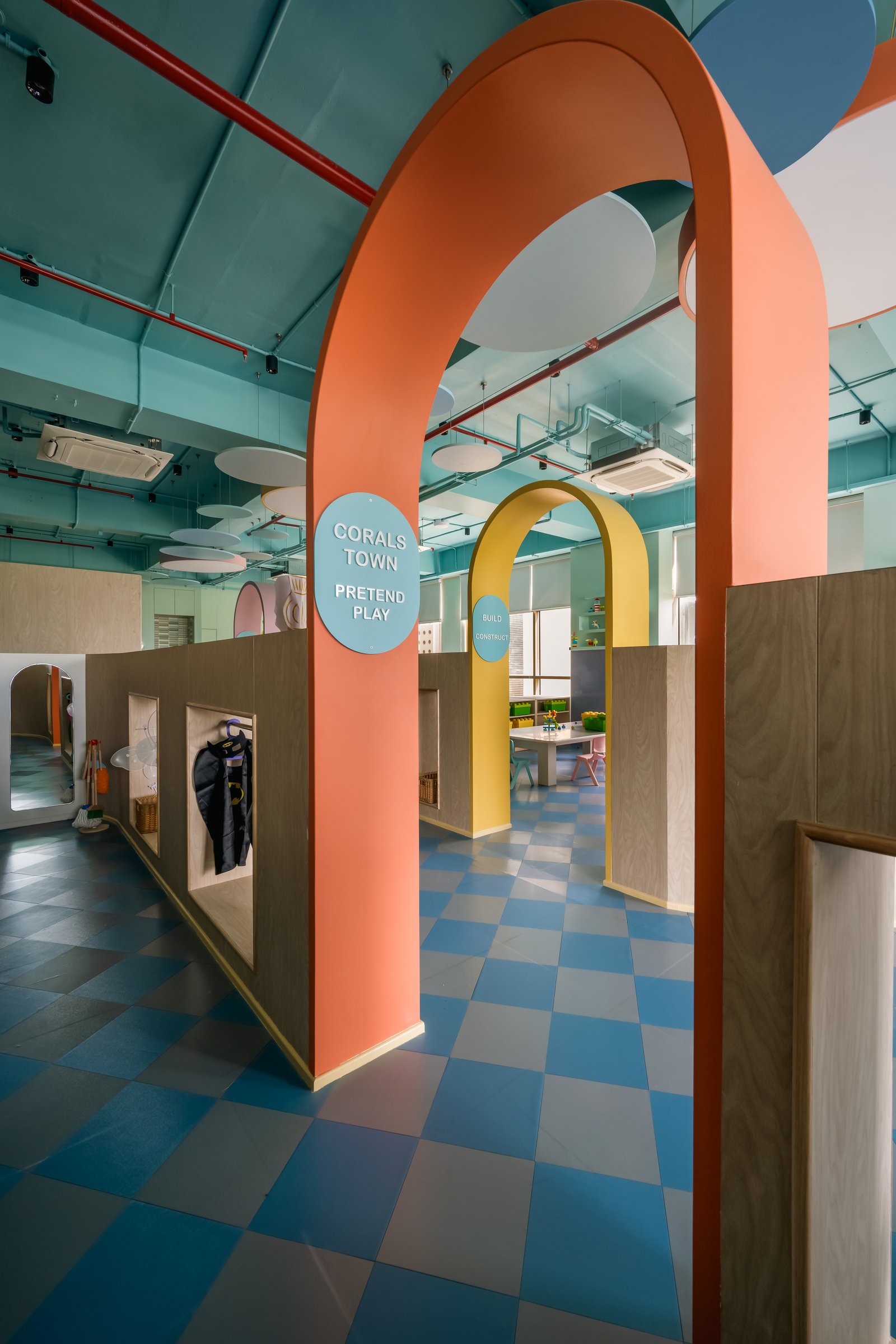 Free-standing arches in coral and ochre treat thresholds as proscenium frames rather than walls