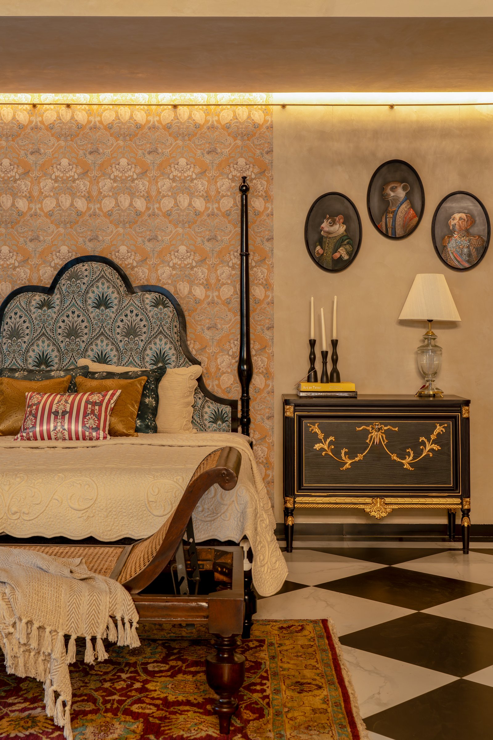 A bedroom set staged as an essay on layering, period, and wit, with a scalloped upholstered headboard against patterned wallpaper