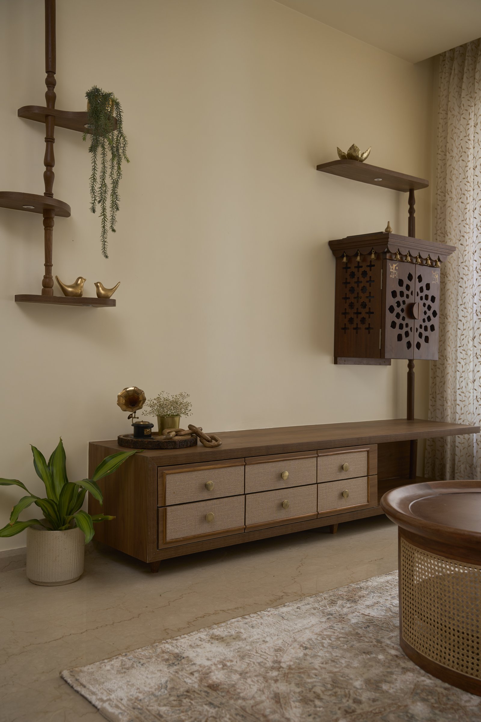 In place of a television wall, an architectural composition of suspended and grounded teakwood columns frames the family mandir
