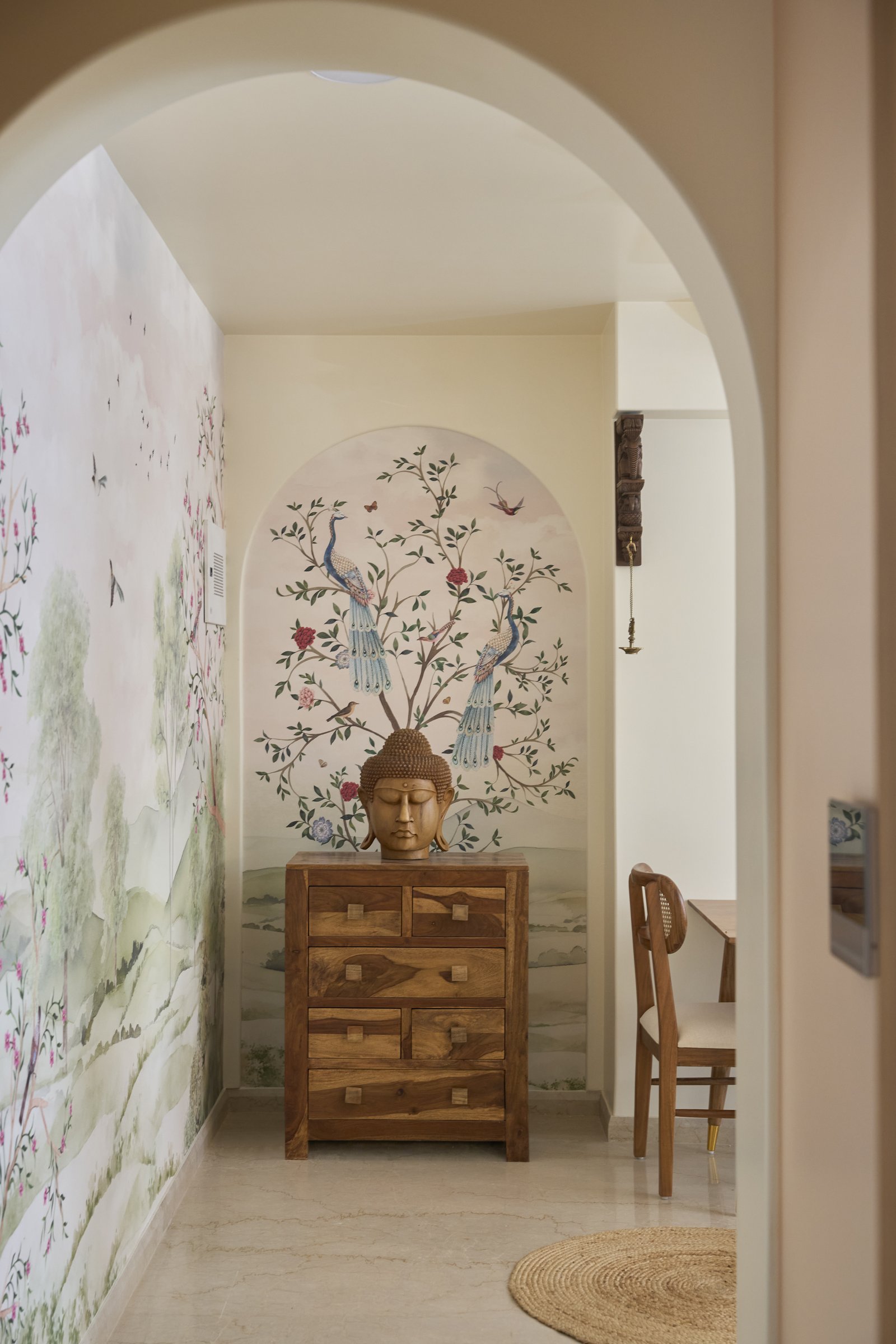 The arrival sequence: a hand-painted peacock mural framed within an arched threshold, anchored by a Buddha on a wooden chest