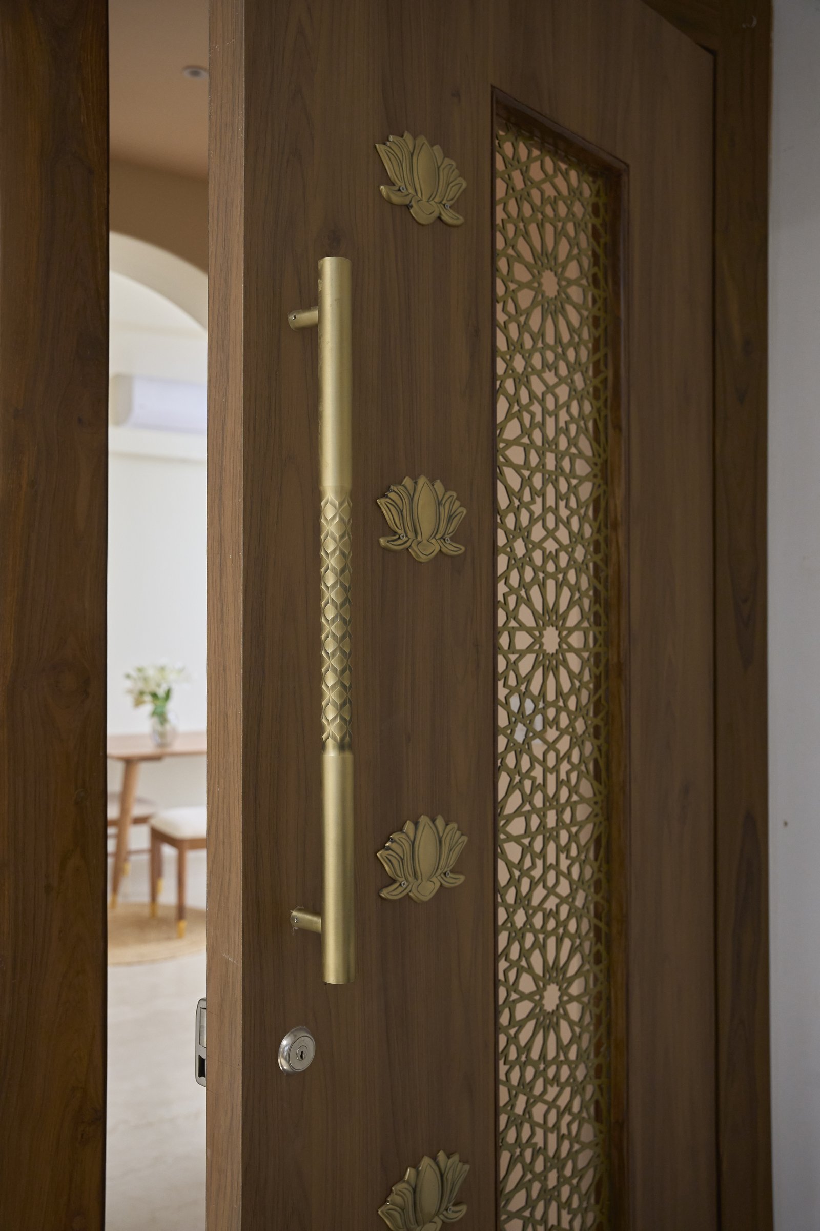 The entrance door, where a brass lotus motif and geometric grill set the home's material vocabulary before one steps inside