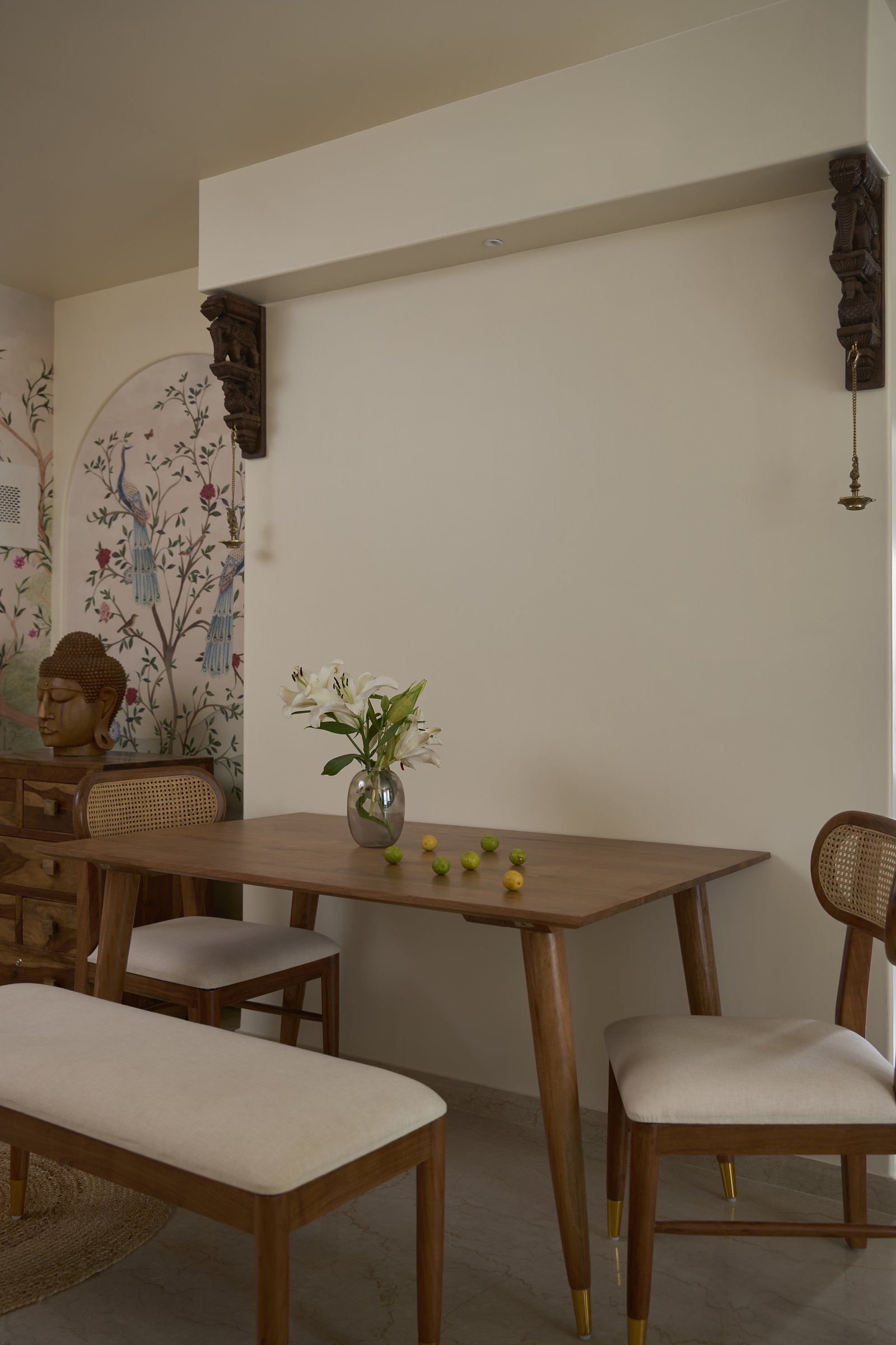 The dining area, sharing its material language with the living room and anchored by a carved corbel and brass diya overhead