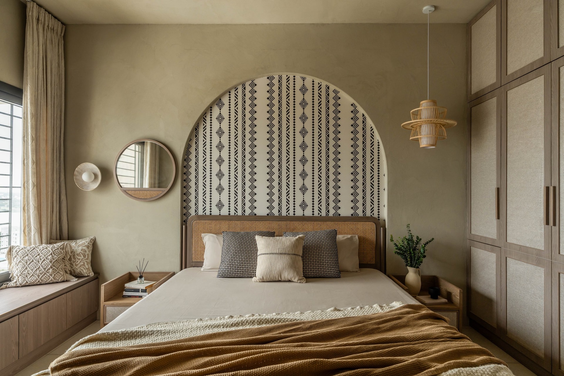 The master bedroom's arched recess holds a graphic wallpaper behind a cane headboard