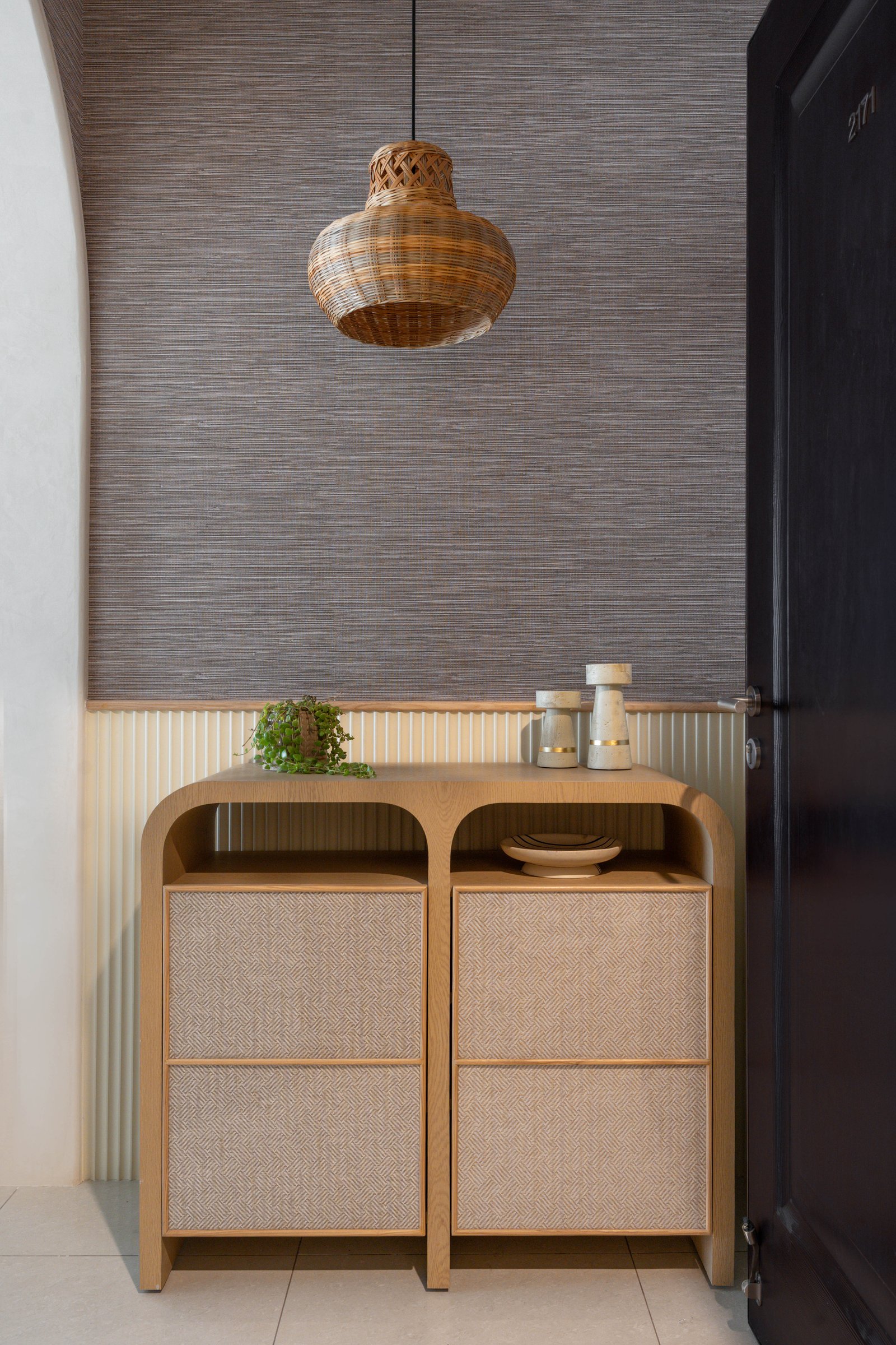 The foyer: grasscloth wallpaper meets fluted panelling above an arched oak-and-cane console, setting the home's material grammar