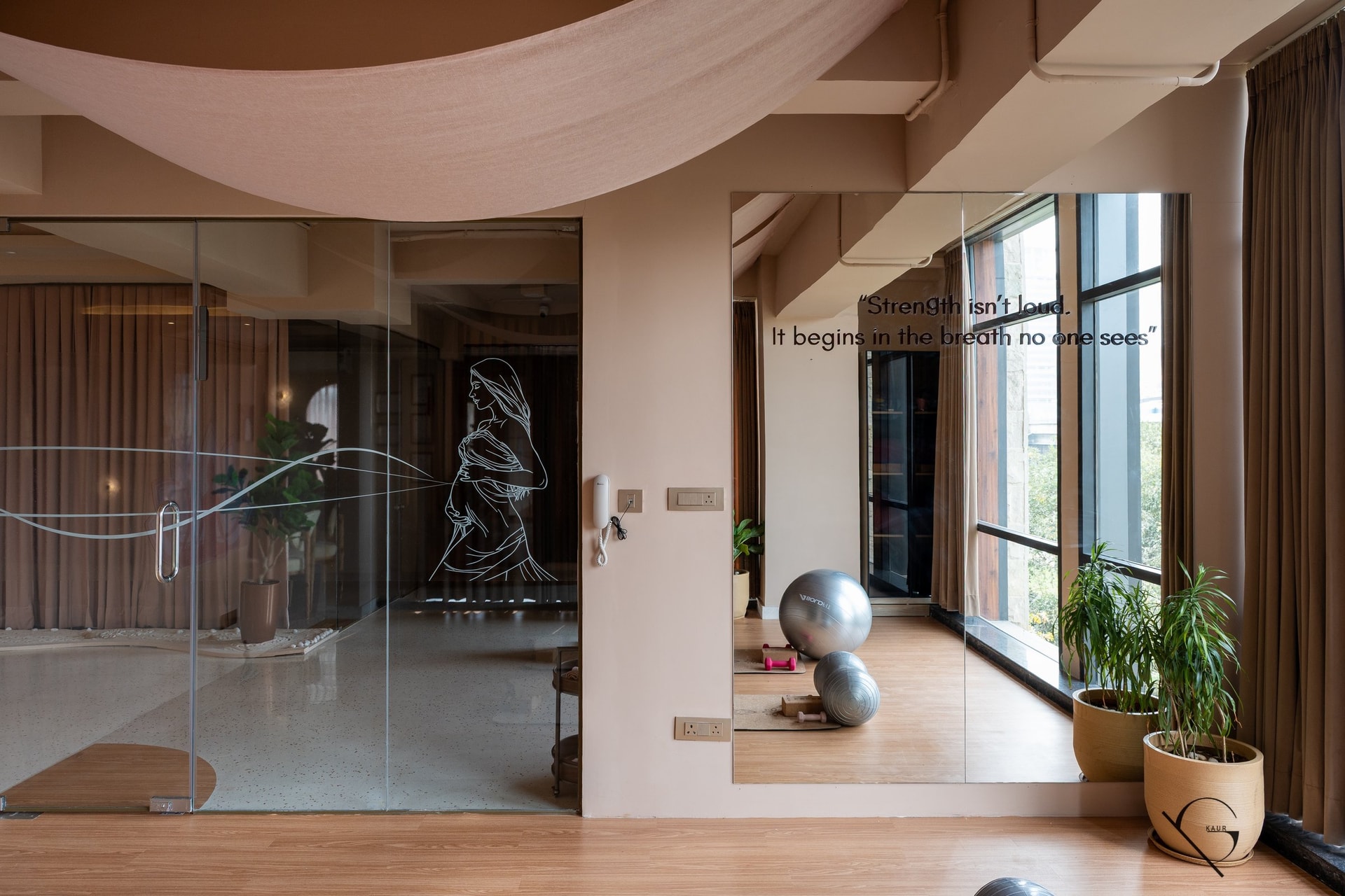 The movement studio: a draped linen canopy softens the ceiling, and an etched glass partition carries the silhouette of a woman in motion