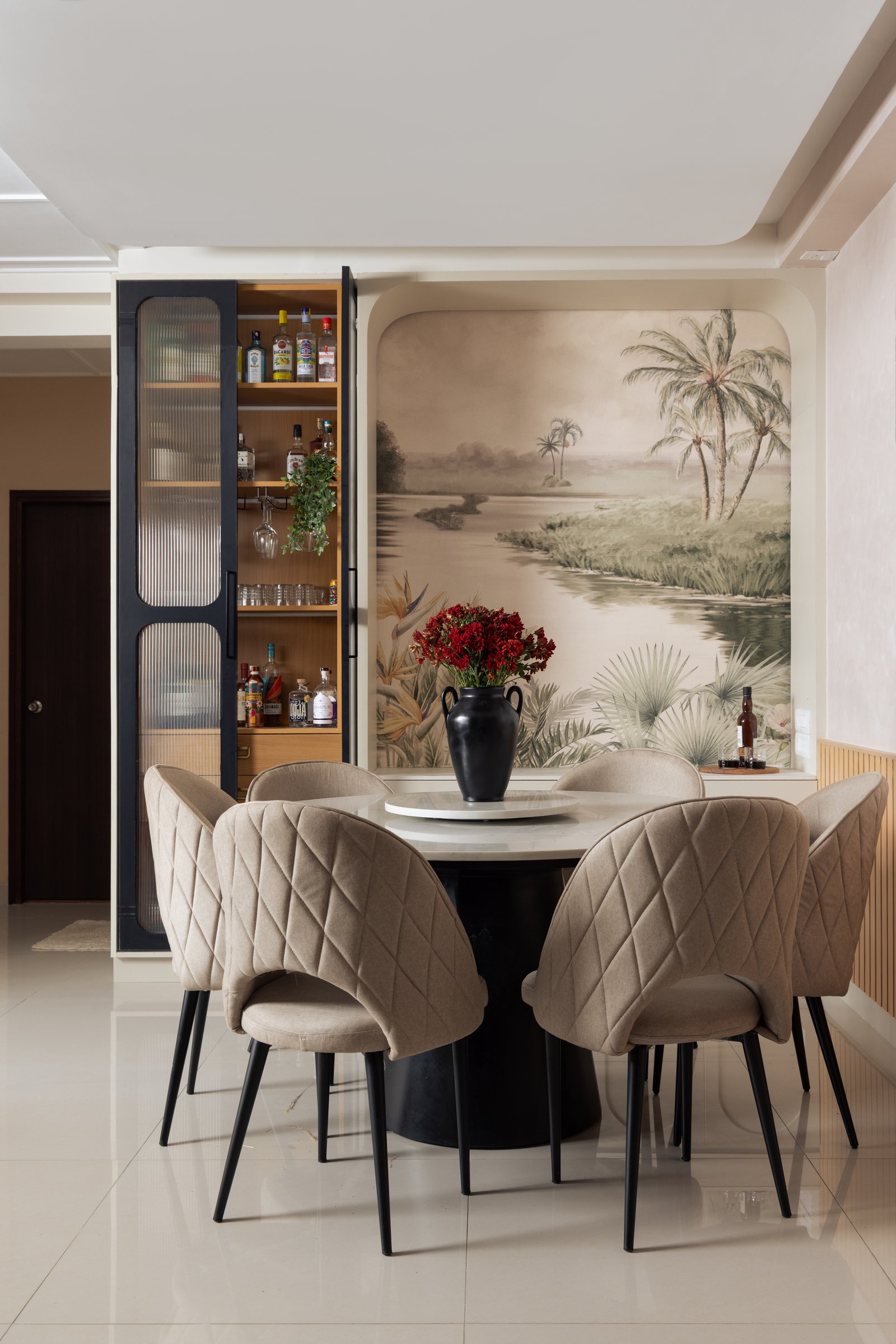 The dining area: a round pedestal table, quilted chairs and a mural-set niche turn a small zone into a staged interlude