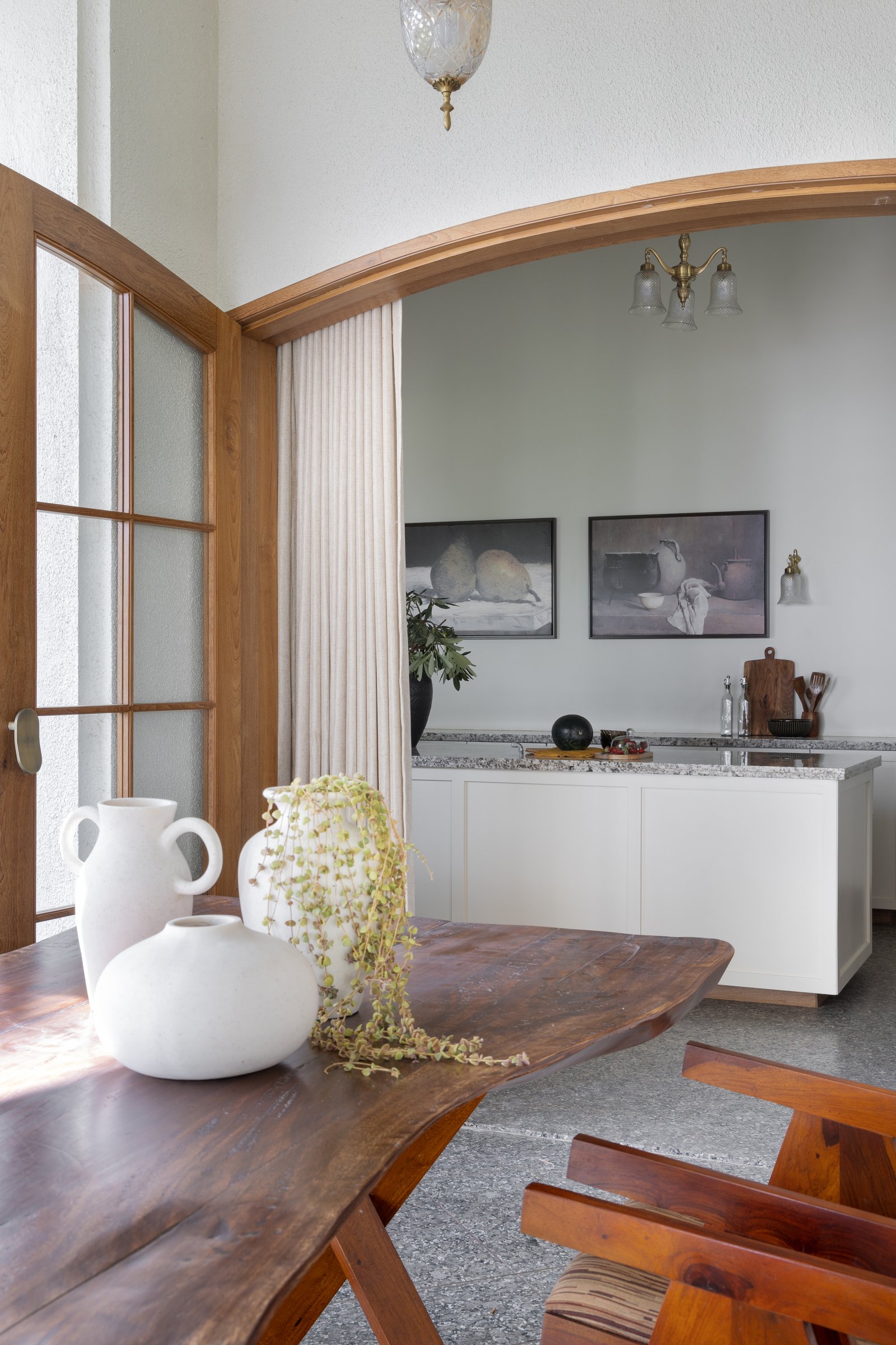 The dining room is staged around a live-edge wooden table, with a taller stained-wood arch opening to the kitchen