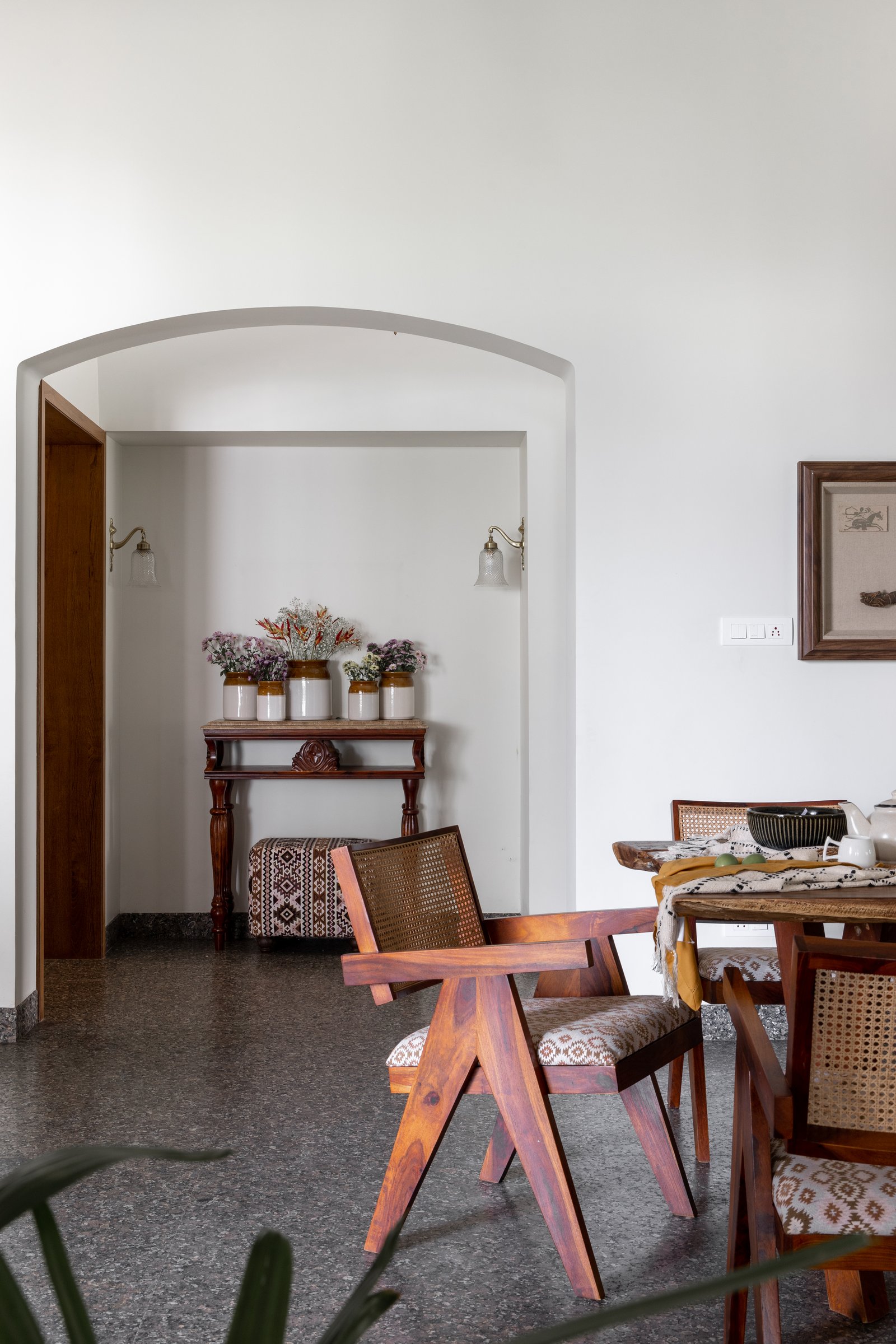 A soft plastered arch frames the entry vignette, anchored by a Chandigarh-language armchair in honey-toned sheesham