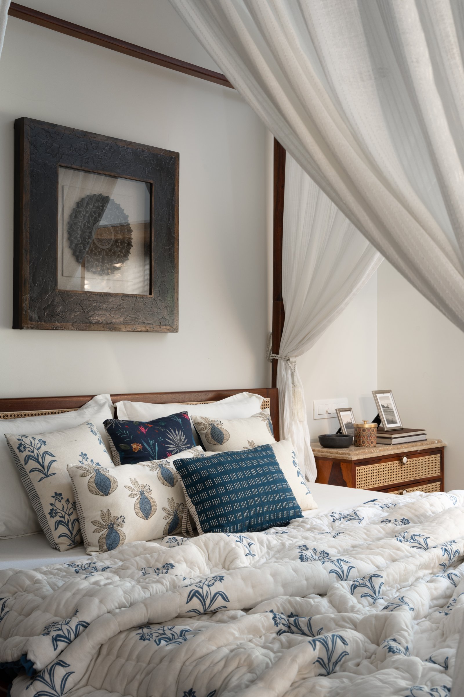 A heavily-textured charcoal artwork and a caned bedside chest layer the headboard wall in quiet detail