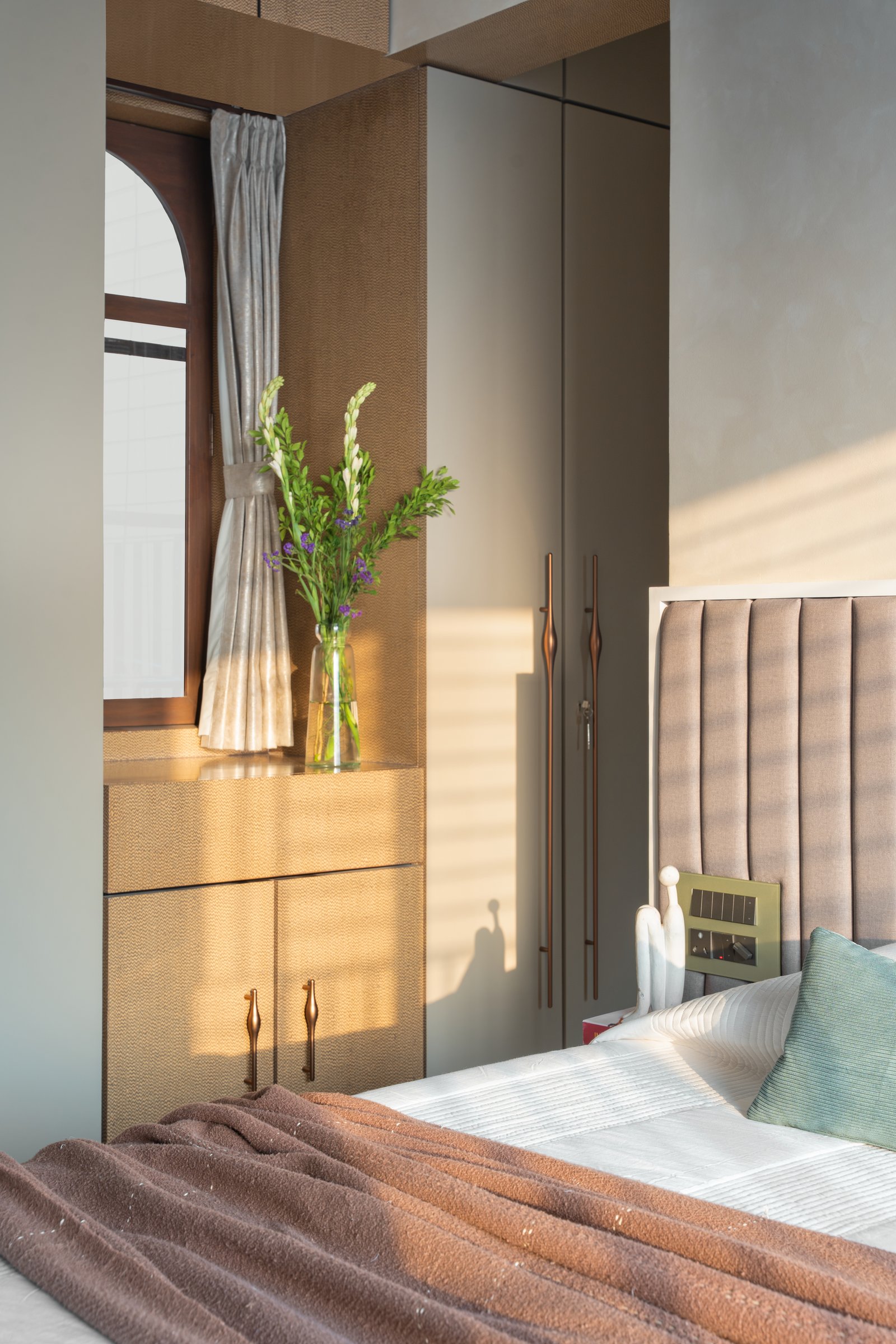 A woven-fabric wardrobe and a slim arched window complete the master's tactile envelope