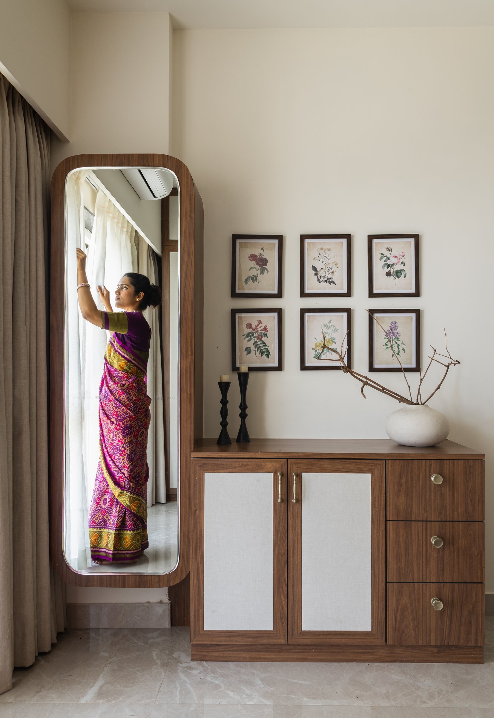 In the parents' bedroom, a softly rounded full-length mirror beside a linen-fronted chest, with six botanical prints above