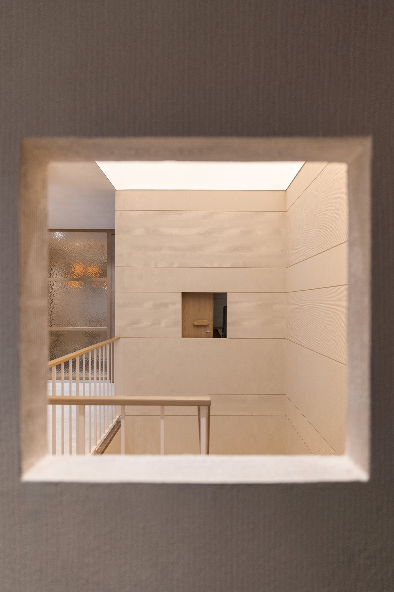 Looking through a framed cut-out at the upper landing, the stair void becomes an unexpectedly vertical shaft of light