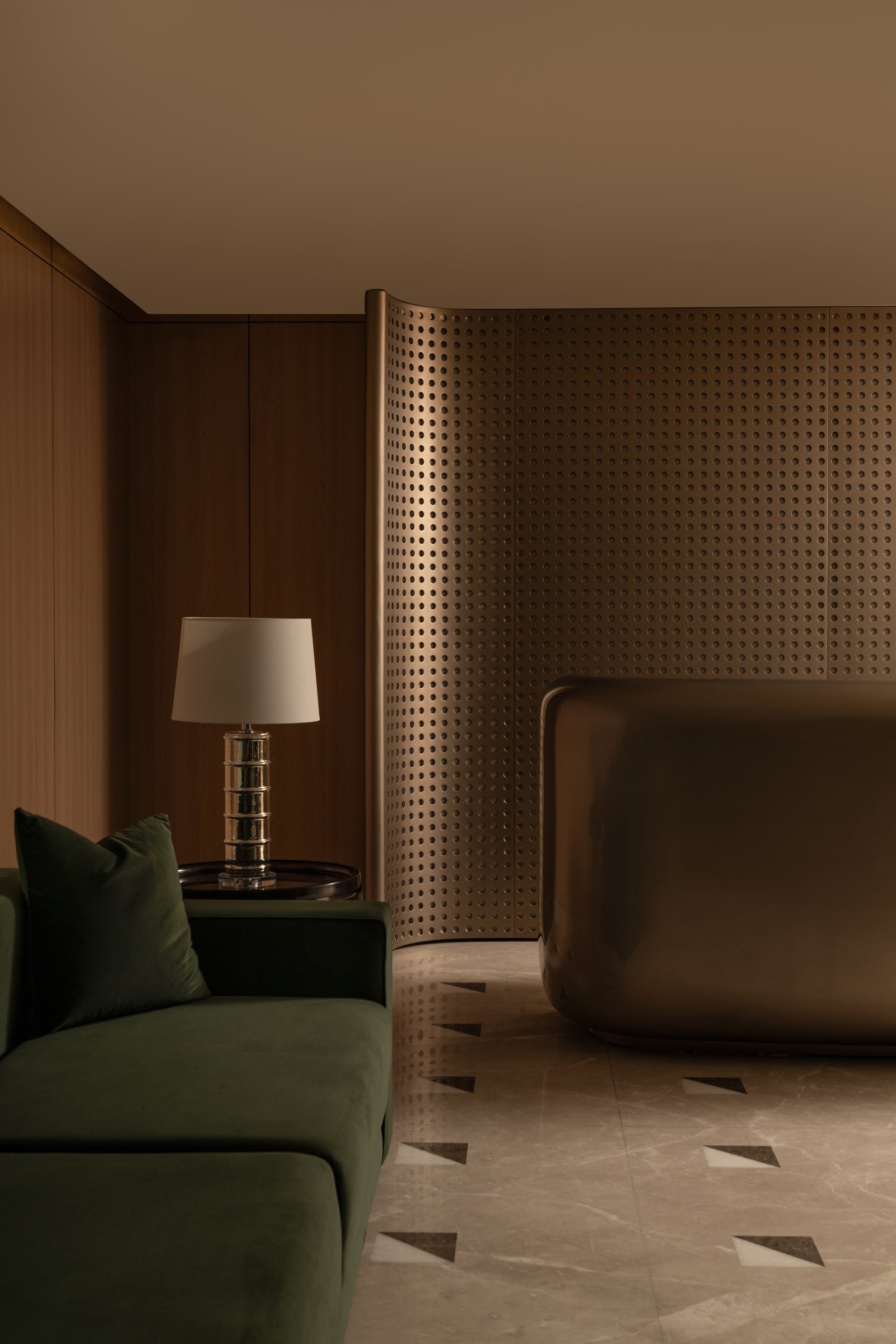 The reception desk: a curved perforated bronze screen wraps a burnished metal counter, partition and sculpture at once