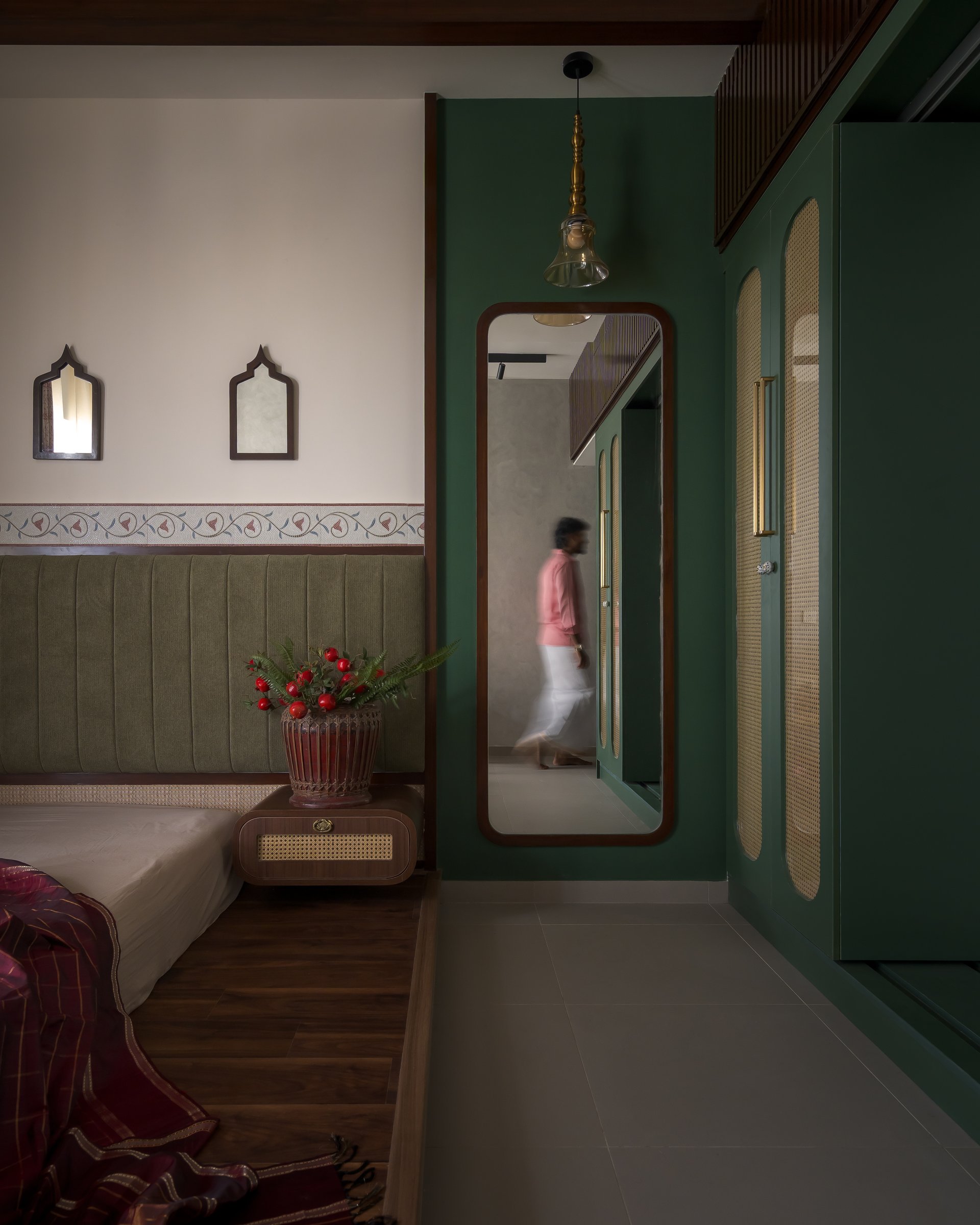The master bedroom's dressing edge, where a full-length mirror and green cane-fronted wardrobes hold the room's quieter register