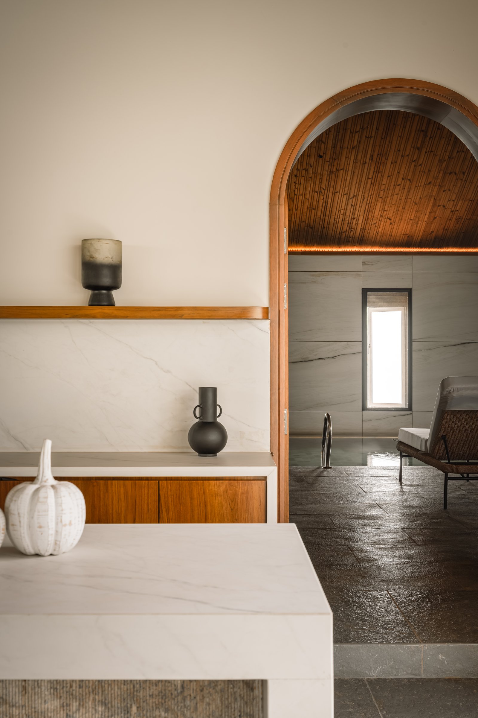 The threshold into the pool pavilion, framed by a warm teak arch and a marble-topped console
