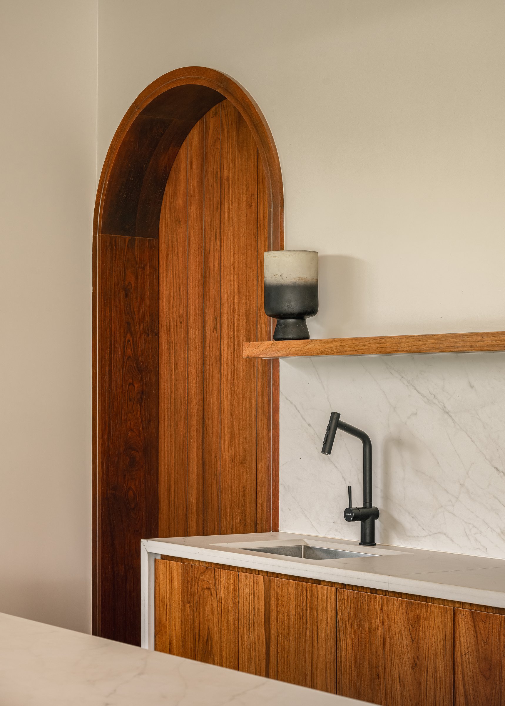 A detail of the counter, where a teak-panelled arch is set into the wall beside the marble backsplash