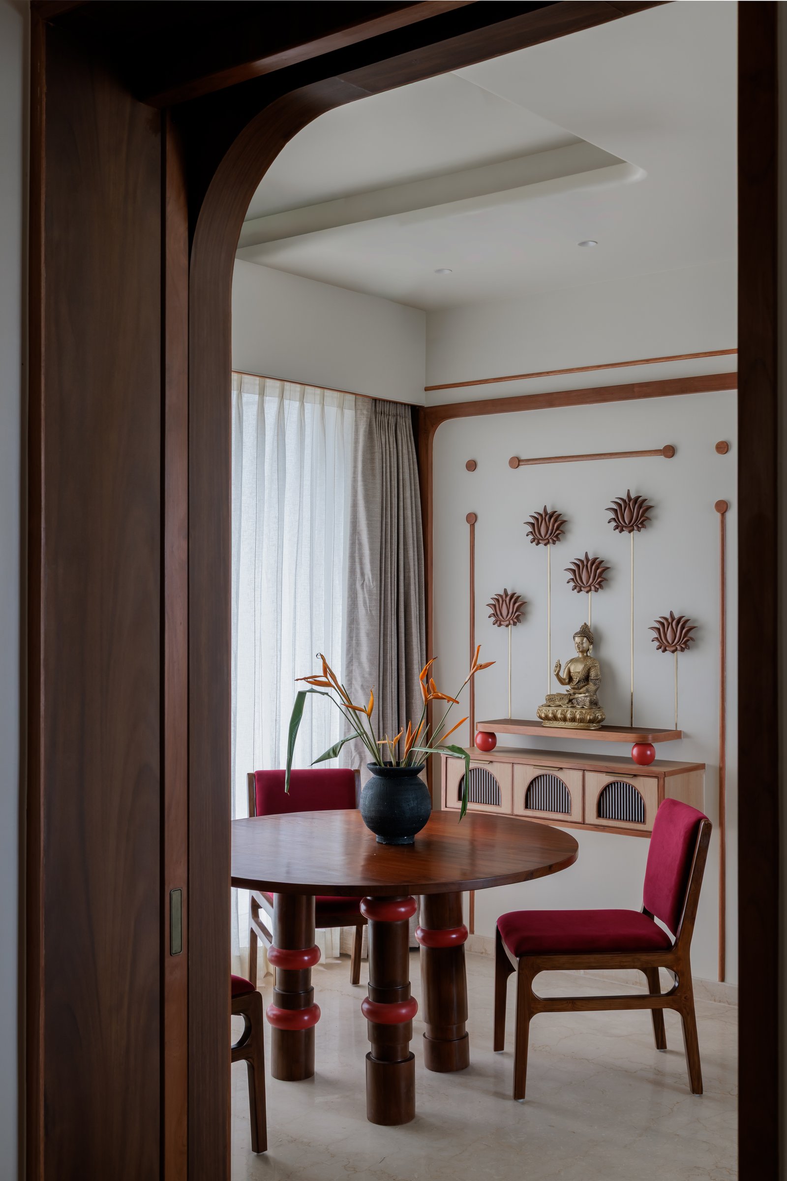 The dining zone, framed by a teak archway with the puja alcove composed behind