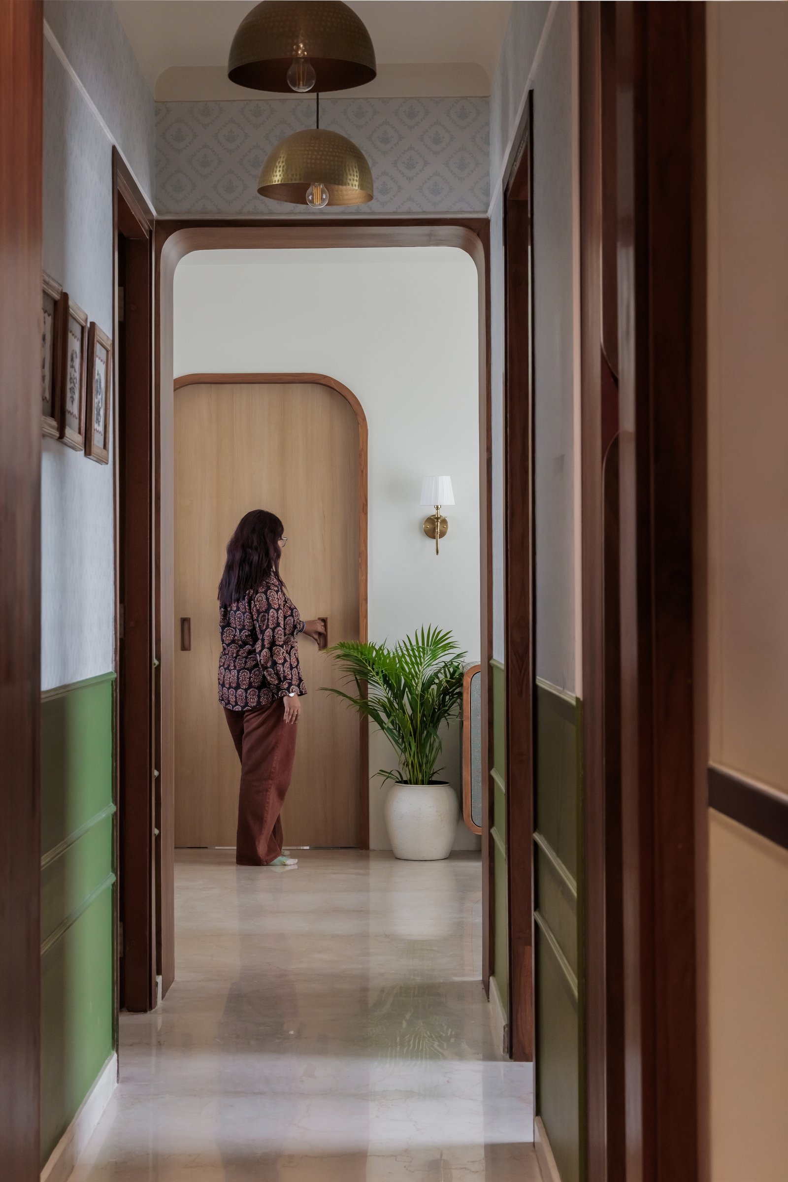 The entry corridor, where a sage green dado and hammered brass pendants introduce the home's material register before any room reveals itself