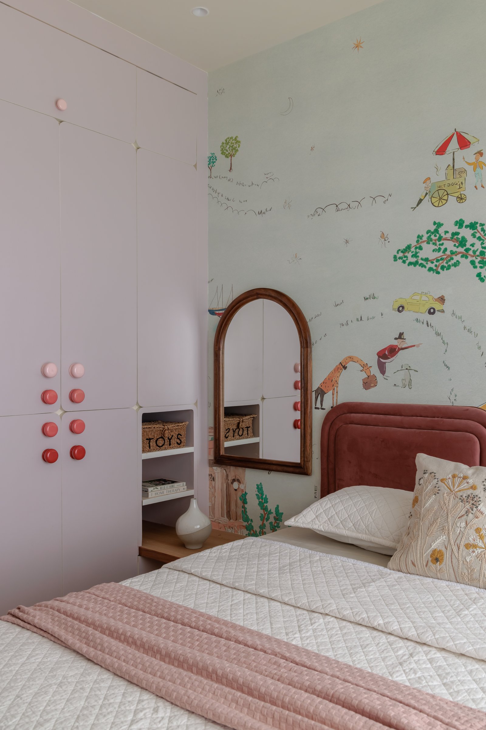 The child's wardrobe, its soft-pink doors punctuated with a graded cluster of red and pink medallion knobs
