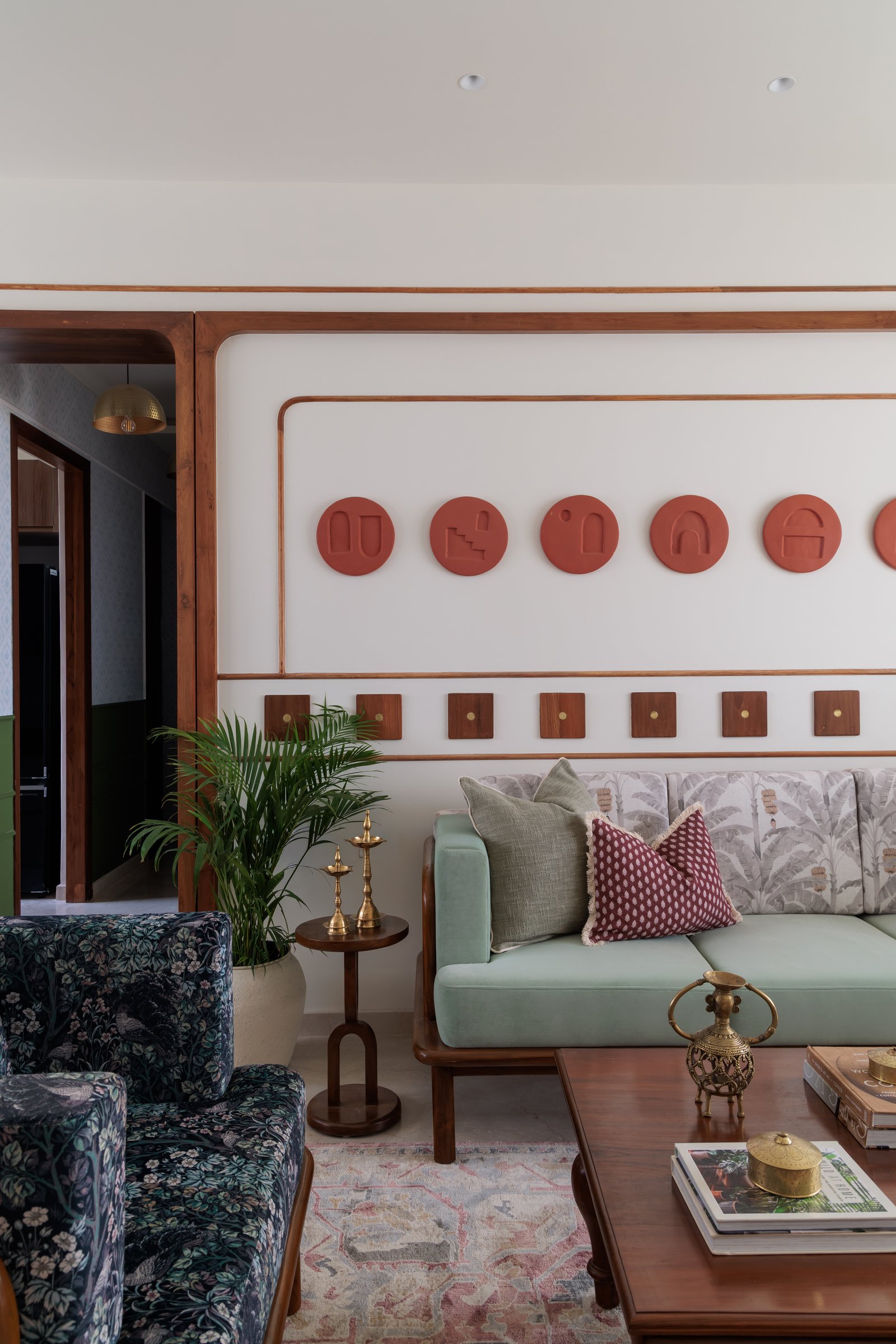 The living room's most articulated wall, where terracotta medallions and small teak plaques compose a quietly collected surface