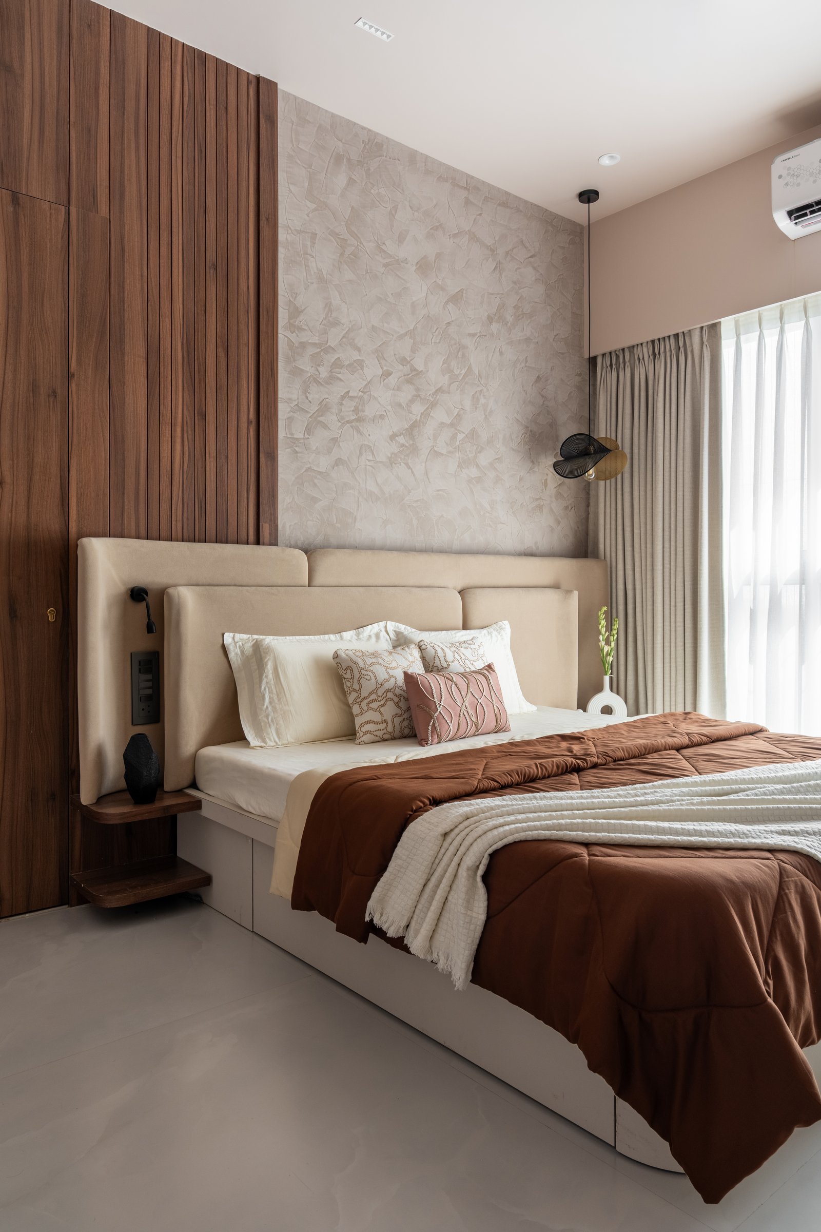 The second bedroom, where a textured plaster feature wall meets dark hardwood panelling behind a low upholstered headboard